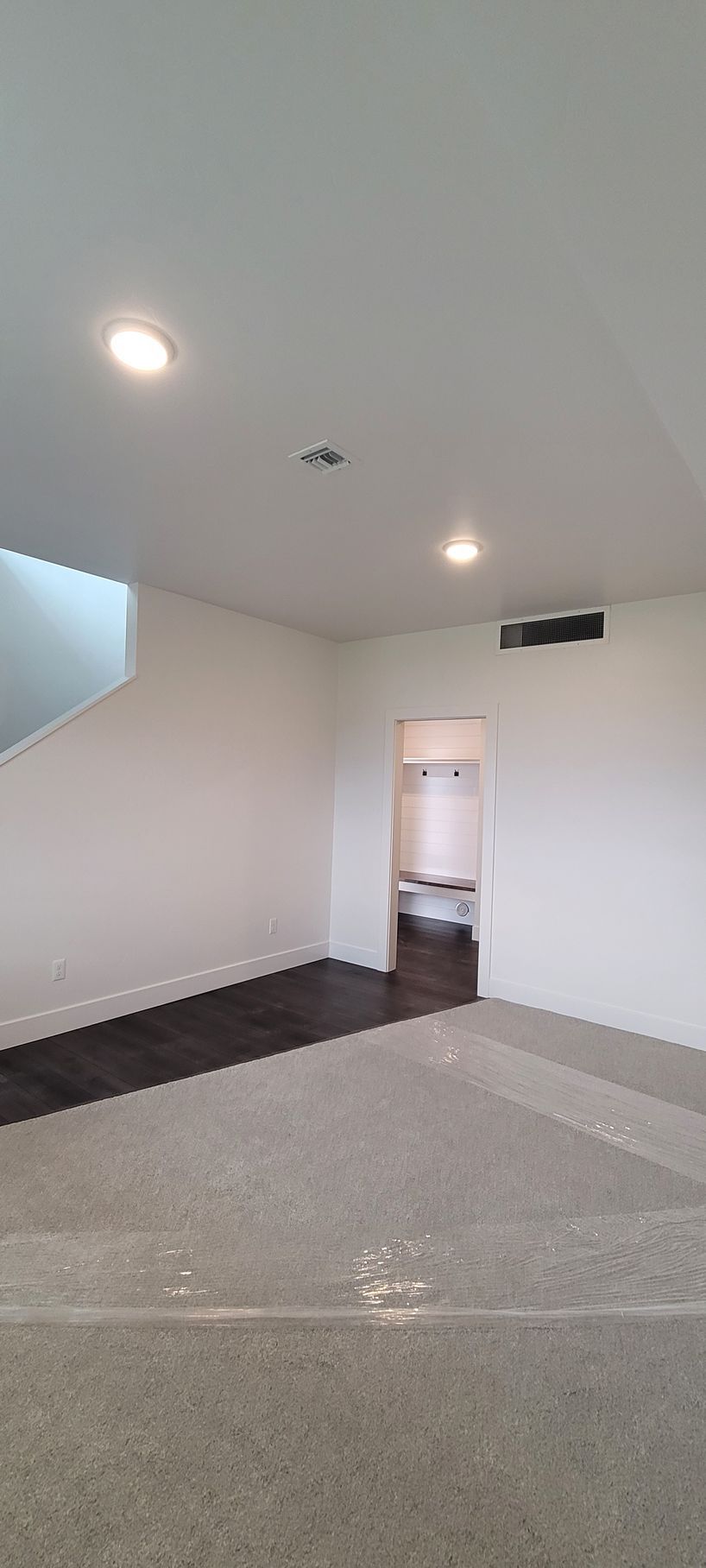 Empty beige room with recessed lights, gray floor, and a doorway to a hallway.