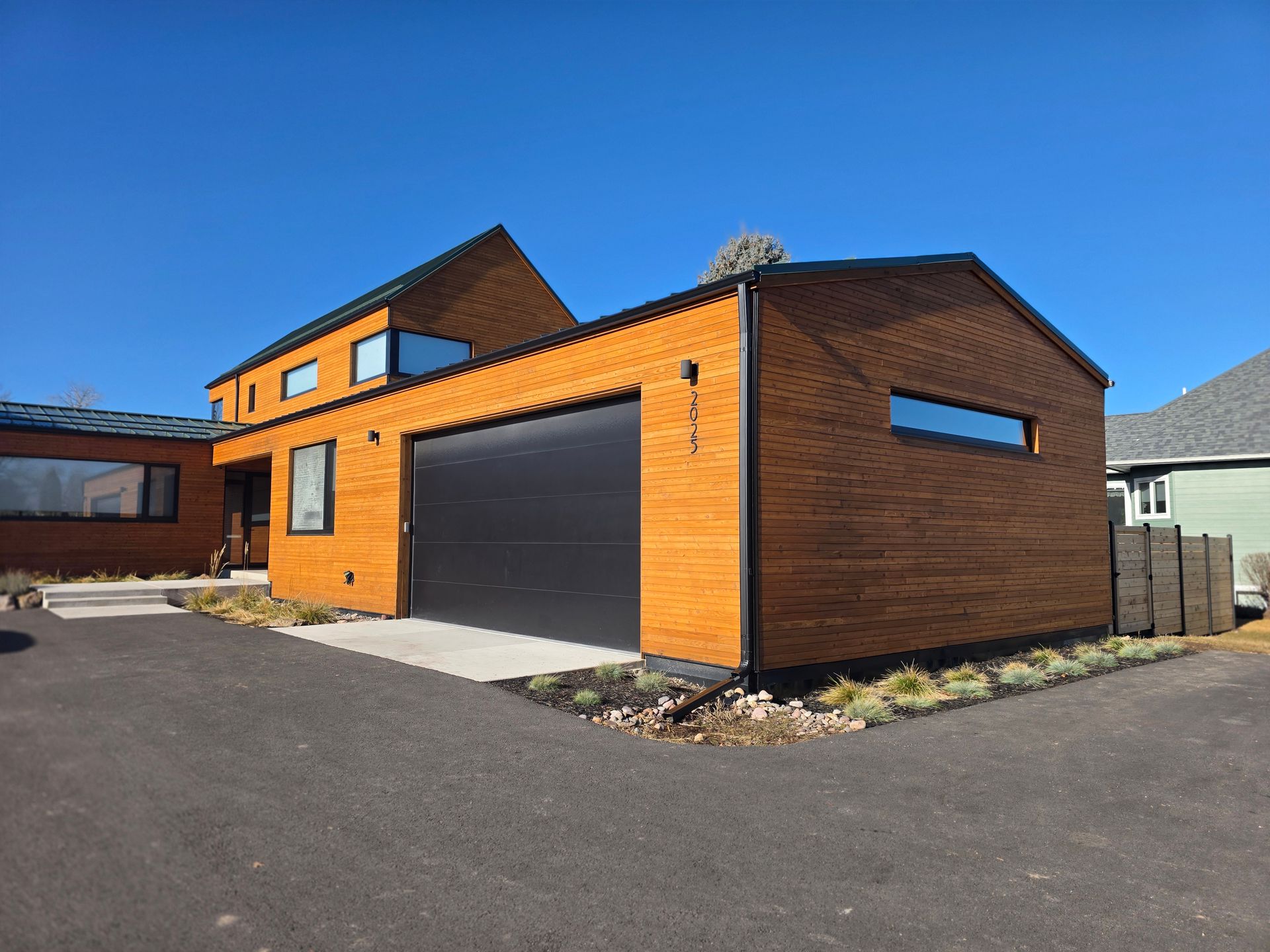 Modern orange brick house with a black garage door and driveway under a clear blue sky