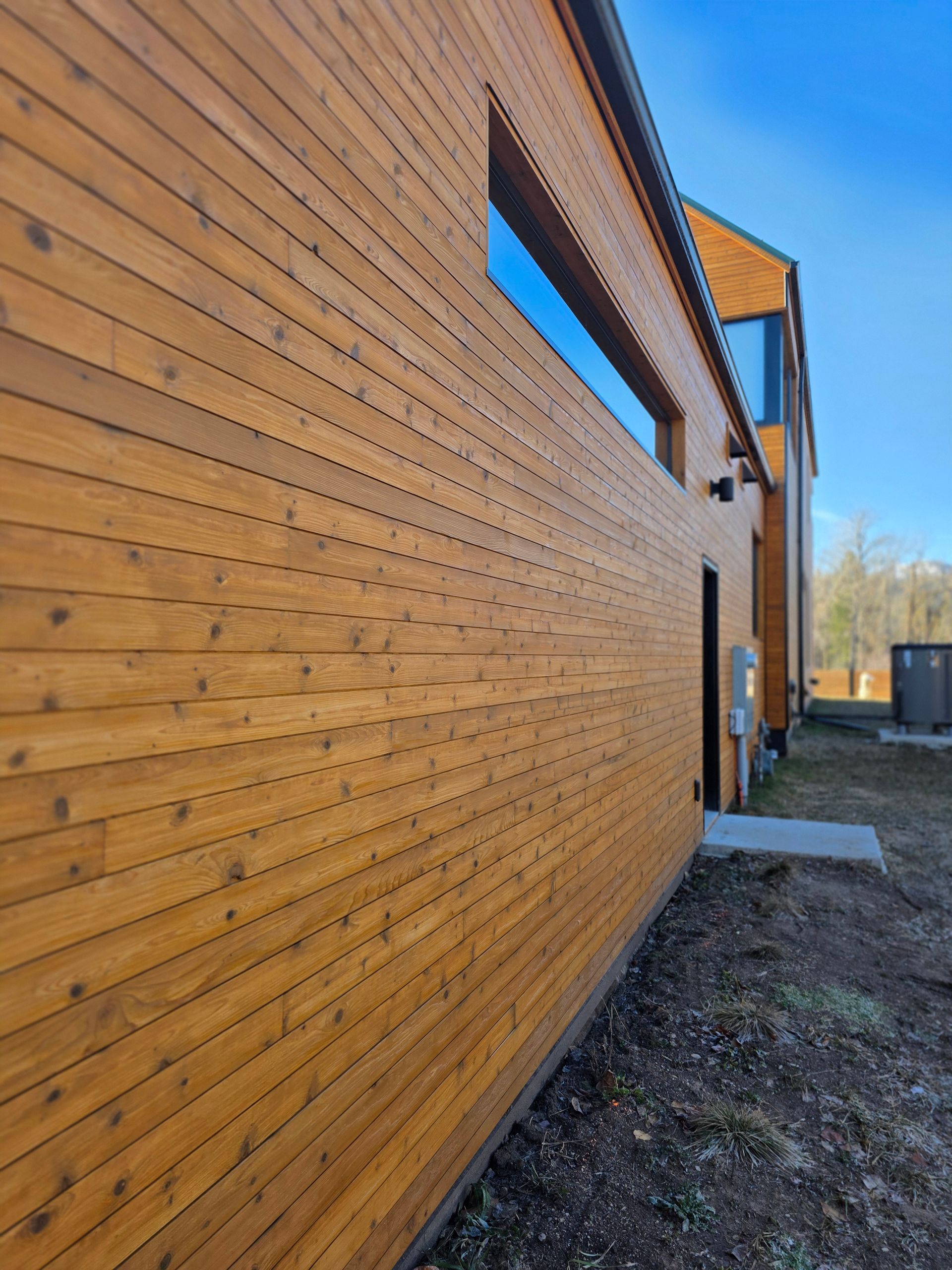Wooden building wall with long windows along a gravel path under a clear blue sky