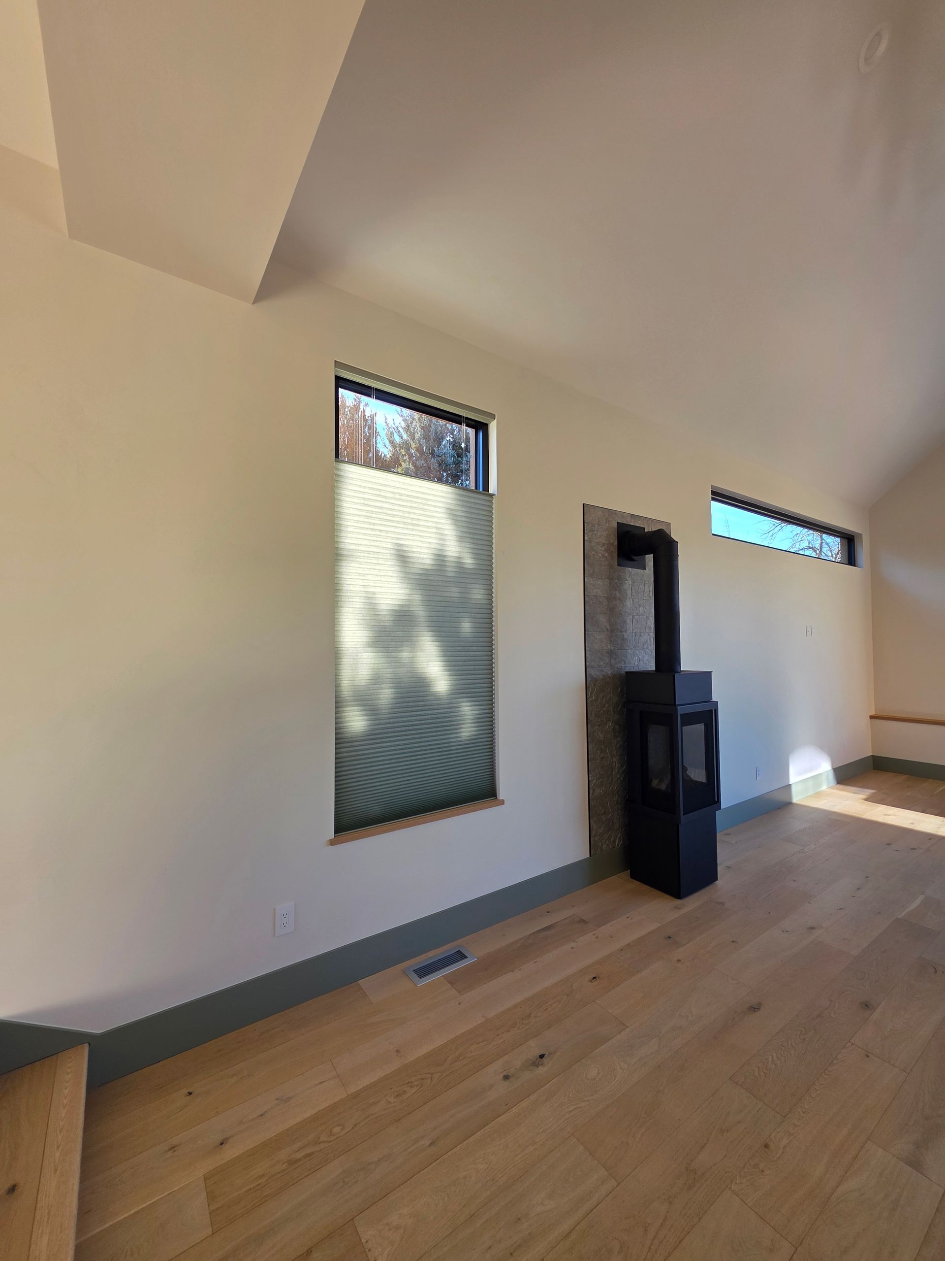 Minimal living room with wood floors, white walls, narrow windows, and a black stove or cabinet against the wall