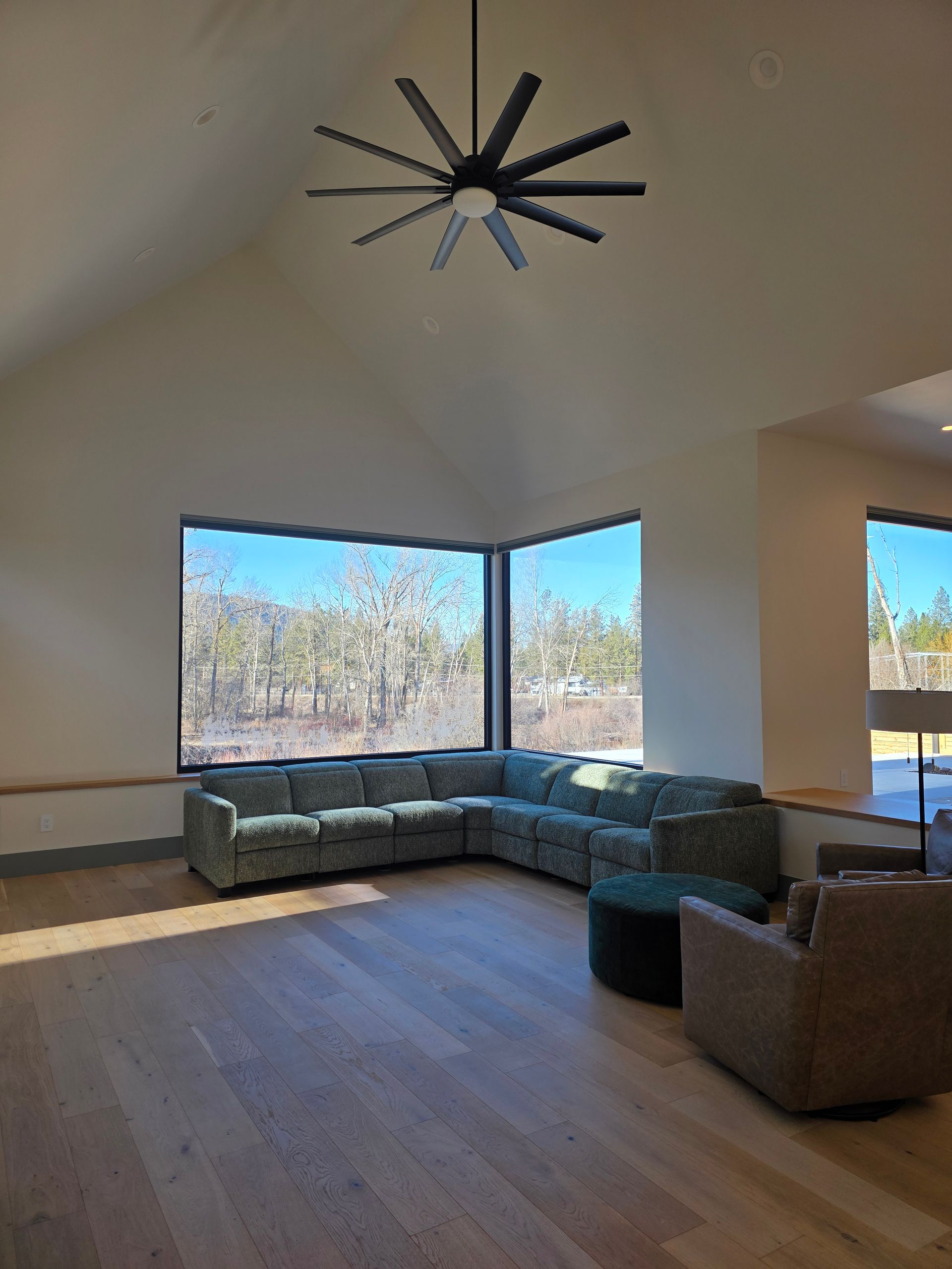 Bright living room with sectional sofa, chairs, and large corner windows overlooking trees and sky.