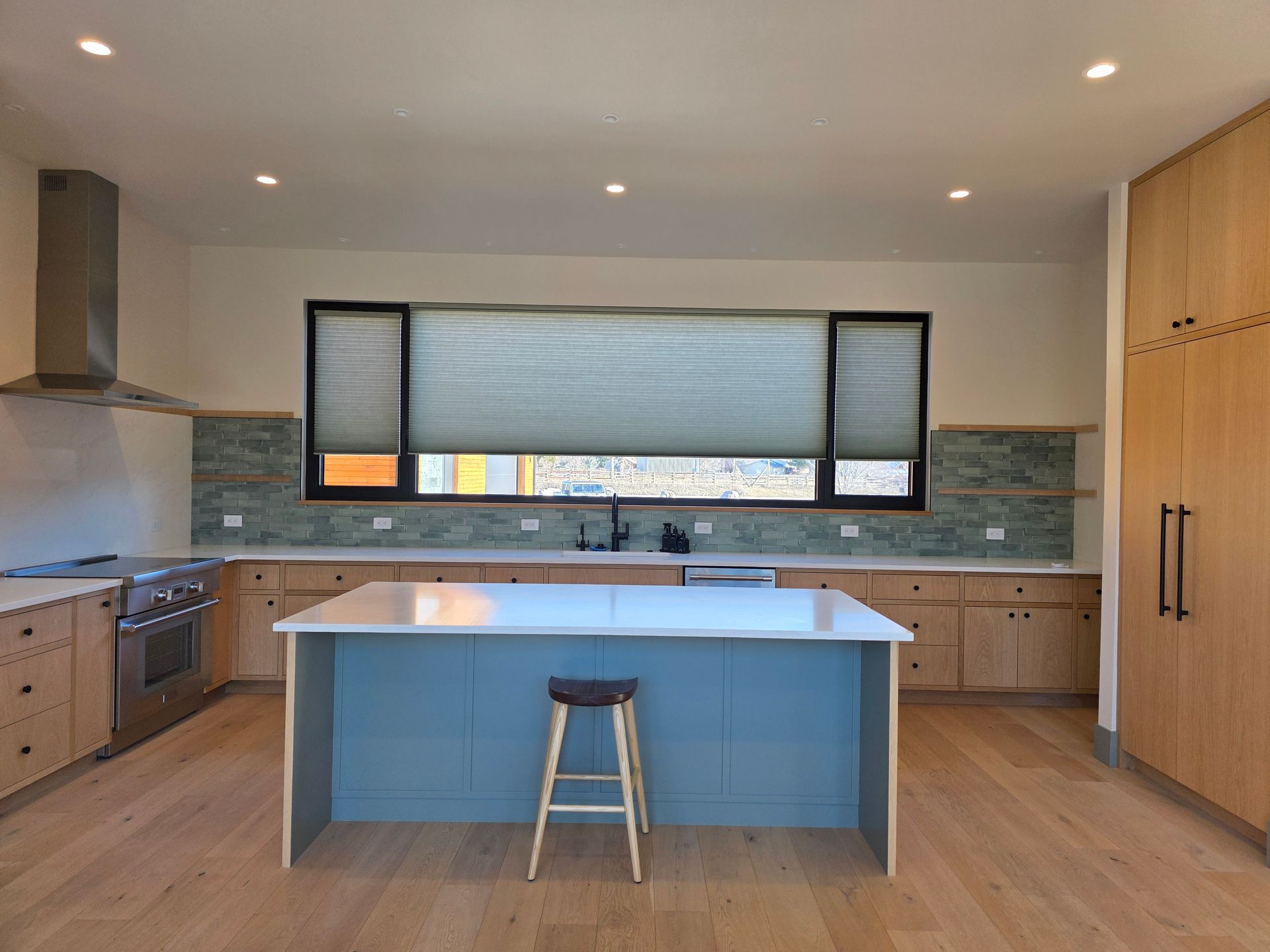 Modern kitchen with blue island, wood cabinets, and a large window above the sink.