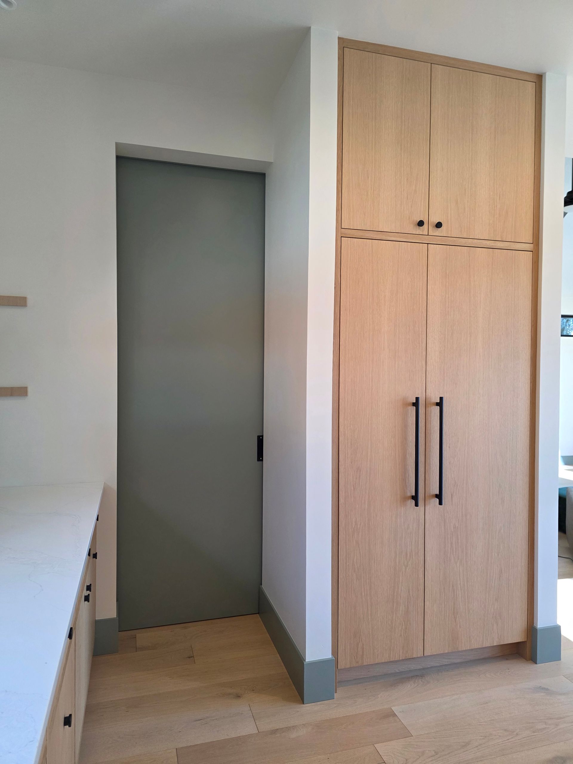Modern kitchen hallway with an open doorway, wood cabinets, and a tall wooden pantry closet