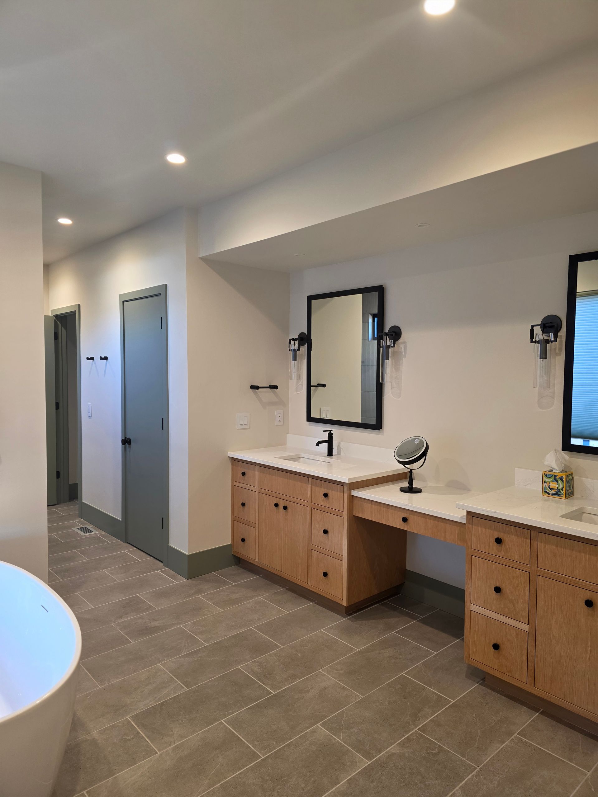 Modern bathroom interior with double vanity, large mirror, gray tiled floor, and stalls in the background