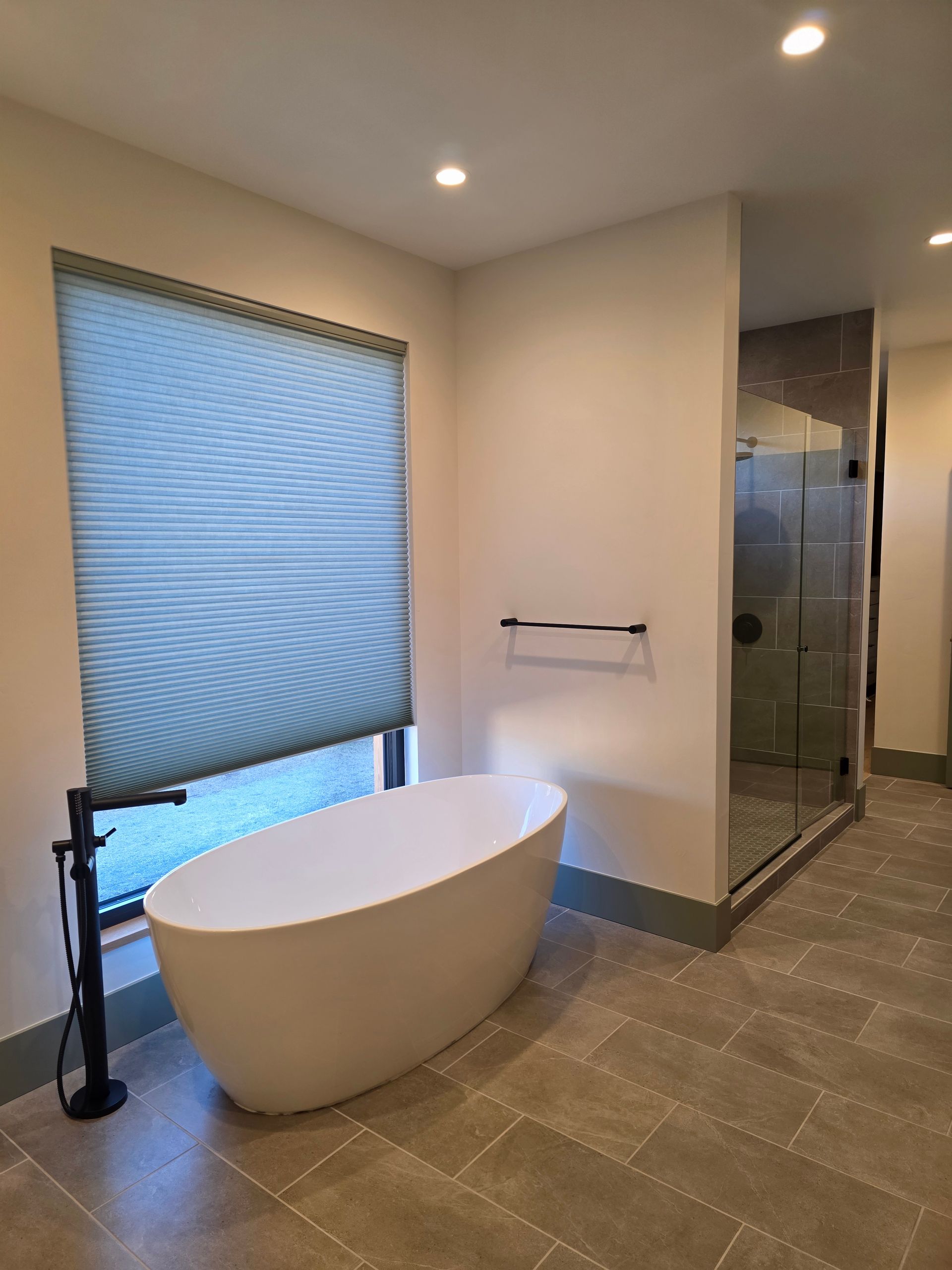 Modern bathroom with freestanding tub, glass shower, towel bar, and window shade