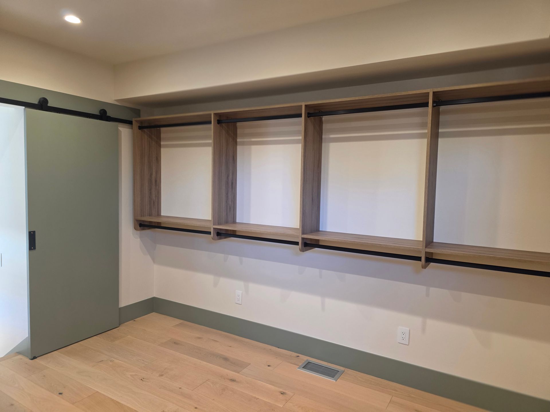 Empty room with light wood floor, beige walls, and built-in wall shelves under a track light.