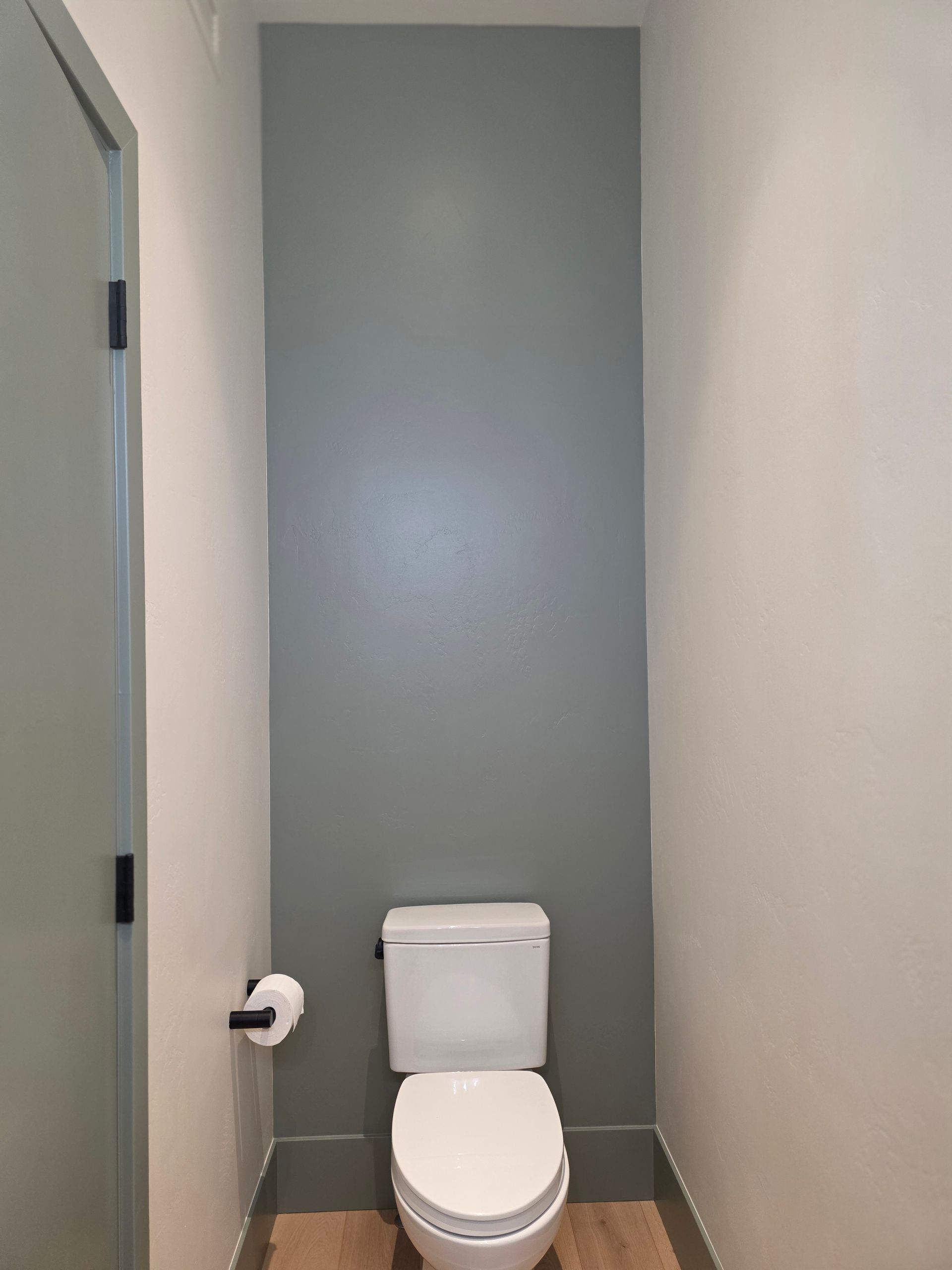 Small bathroom with a white toilet centered against a gray wall and a closed door on the left.