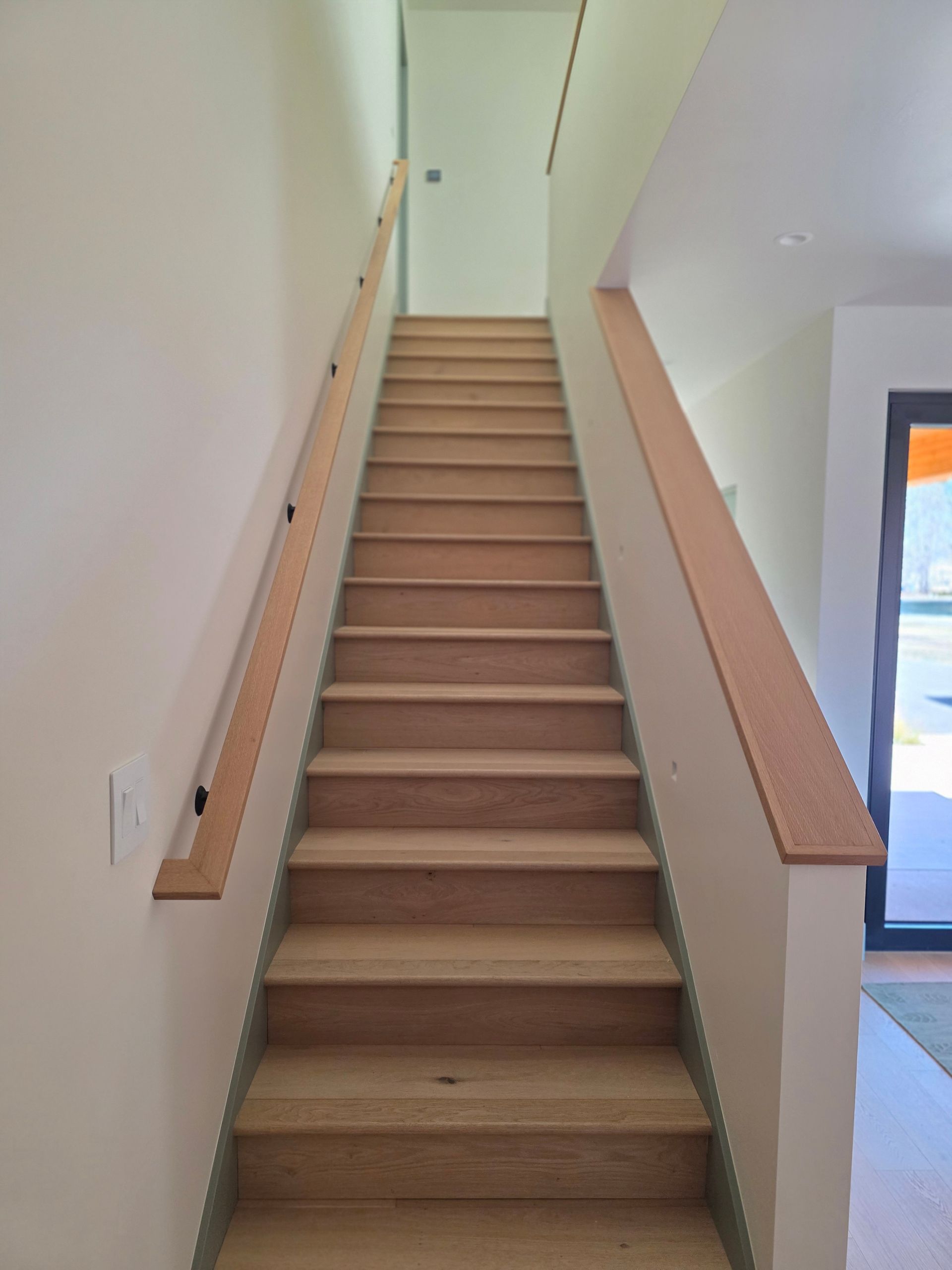Narrow indoor staircase with beige carpet, wooden handrails, and white walls leading to an upper door.
