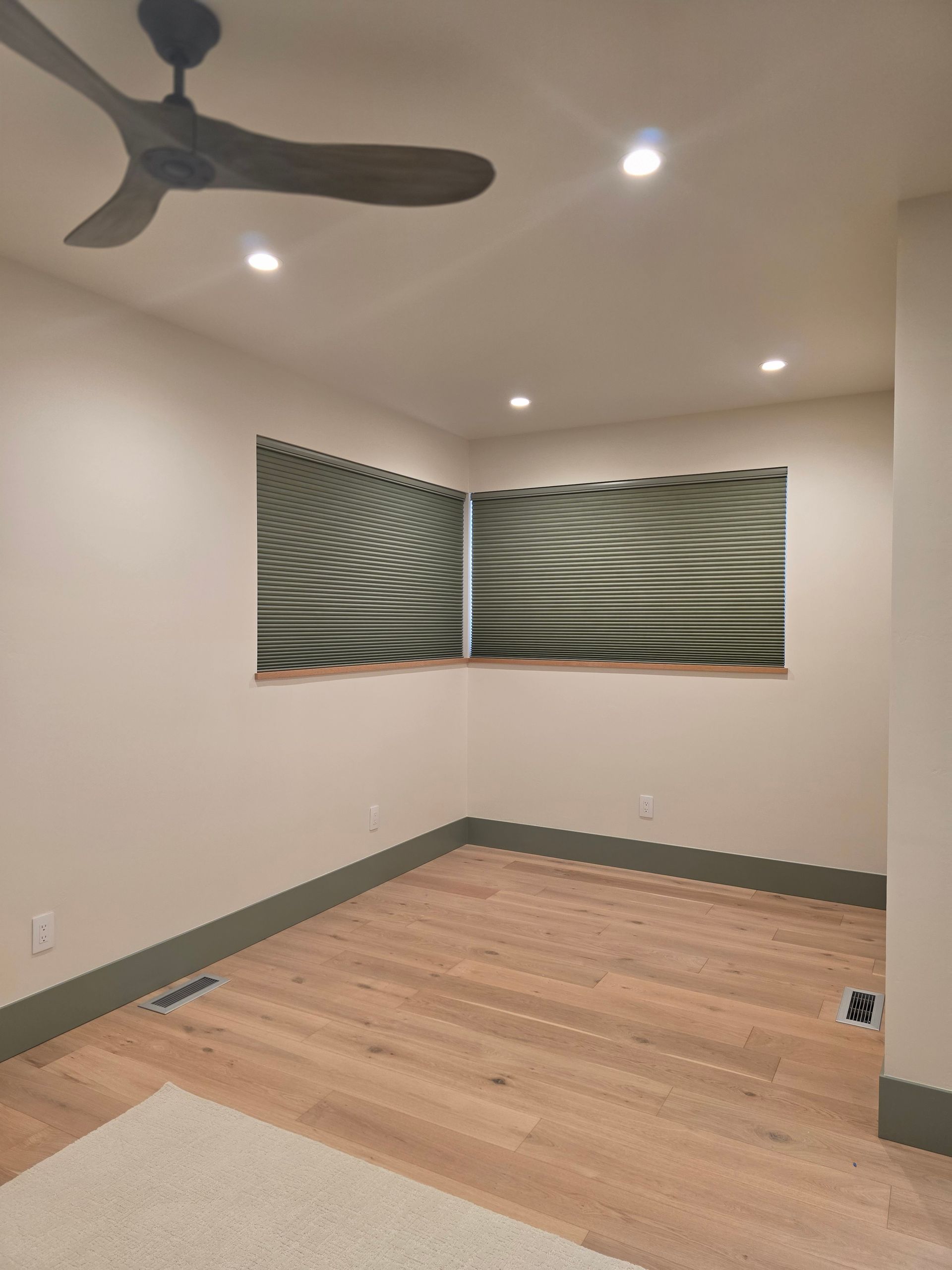 Empty beige room with wood floor, ceiling fan, recessed lights, and abstract wall art.
