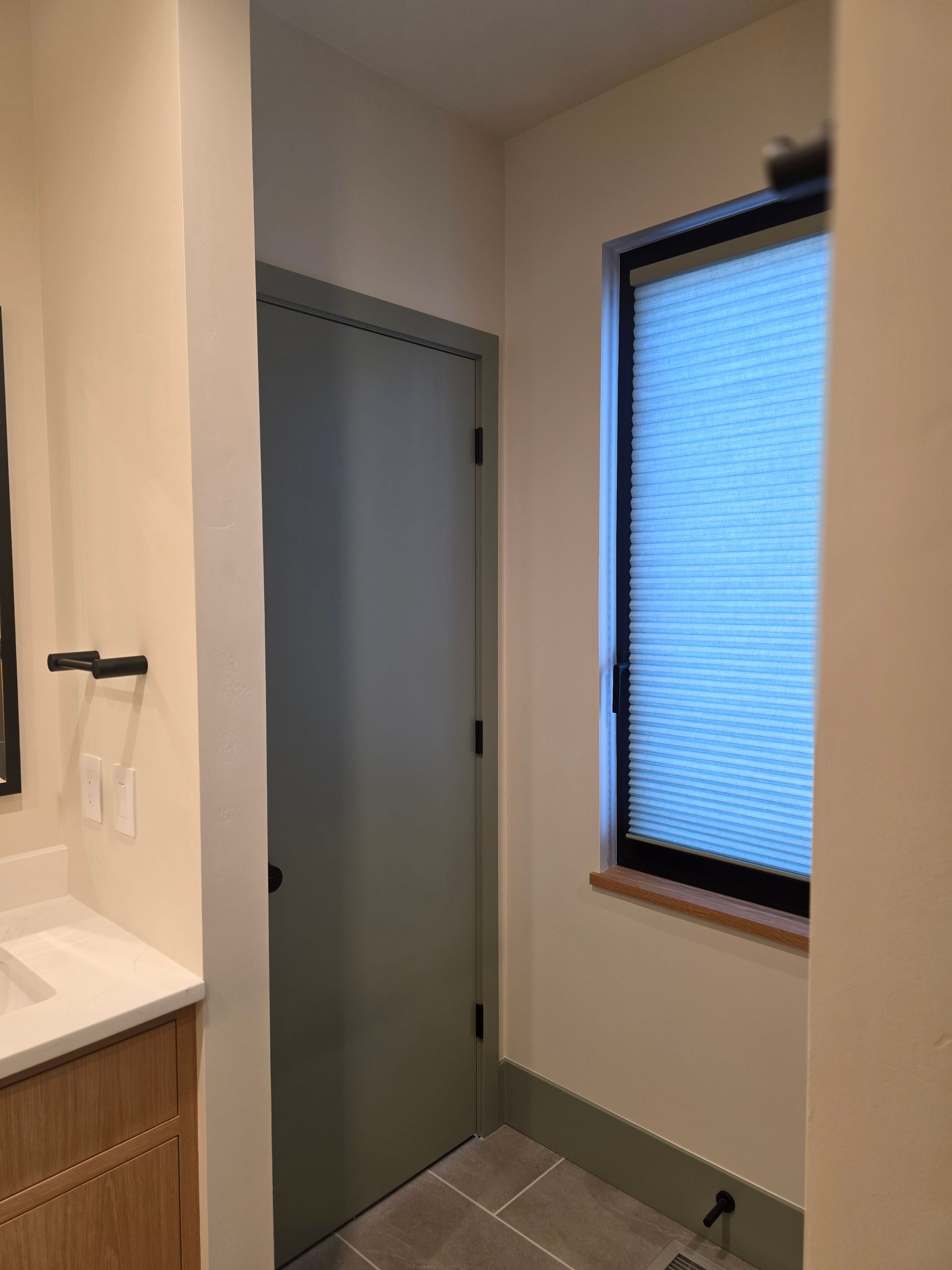 Small bathroom corner with a frosted window, gray door, and beige walls.