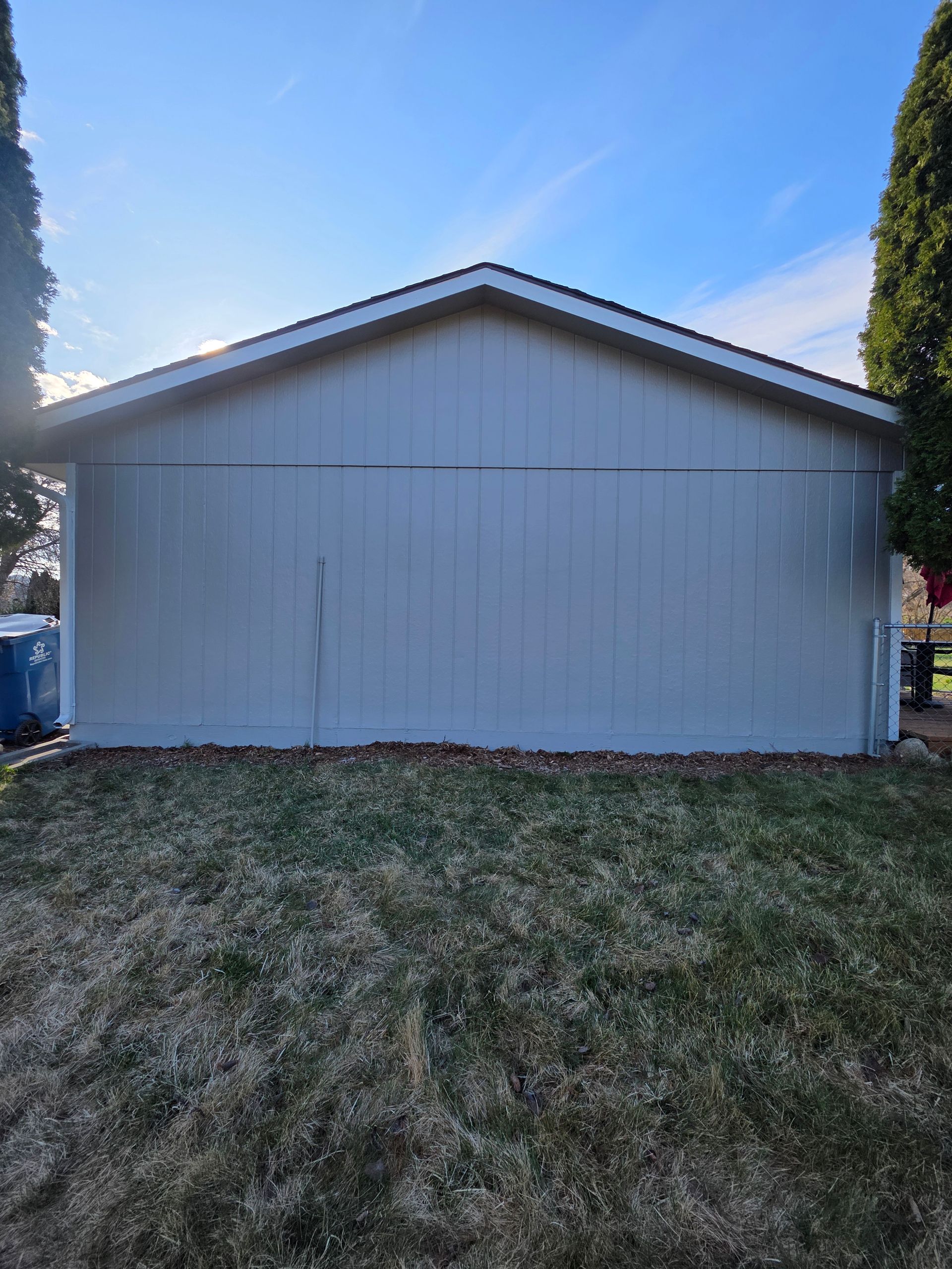 White-sided shed with a gabled roof in a grassy yard under a blue sky.