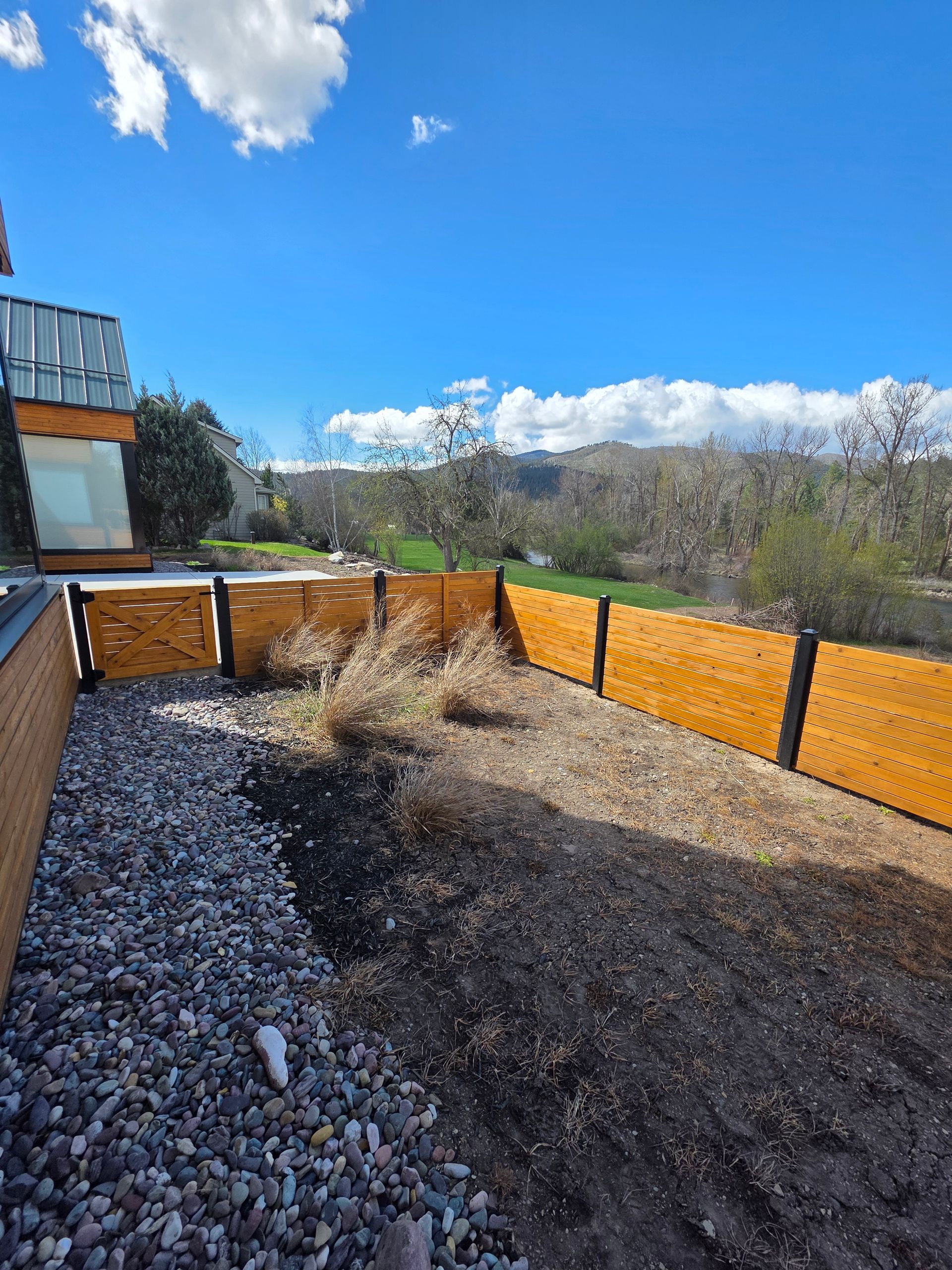 Backyard patio with orange privacy fence, gravel ground, and blue sky with clouds