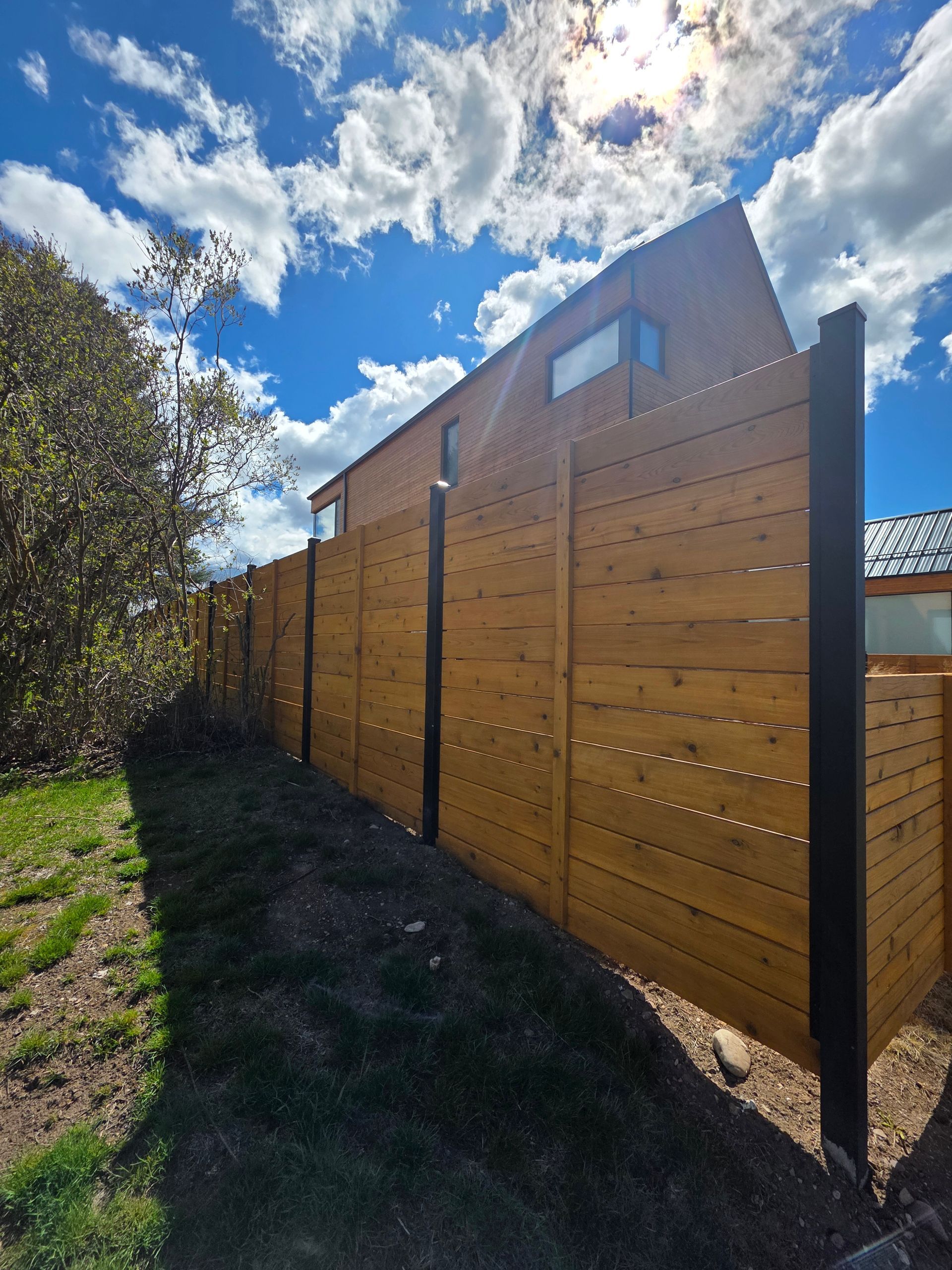 Sunlit wooden privacy fence along a grassy yard under a blue sky with clouds