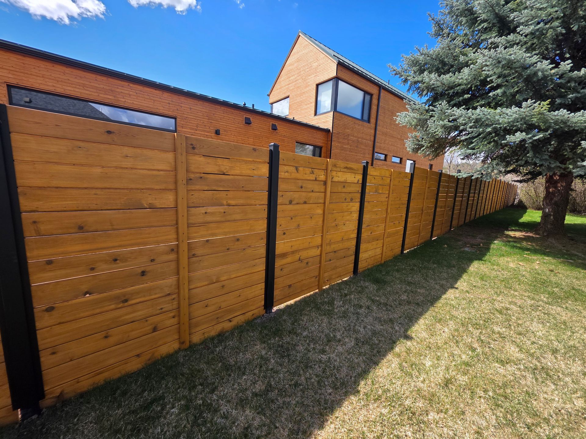 Long wooden fence with black posts beside a grassy yard under a blue sky