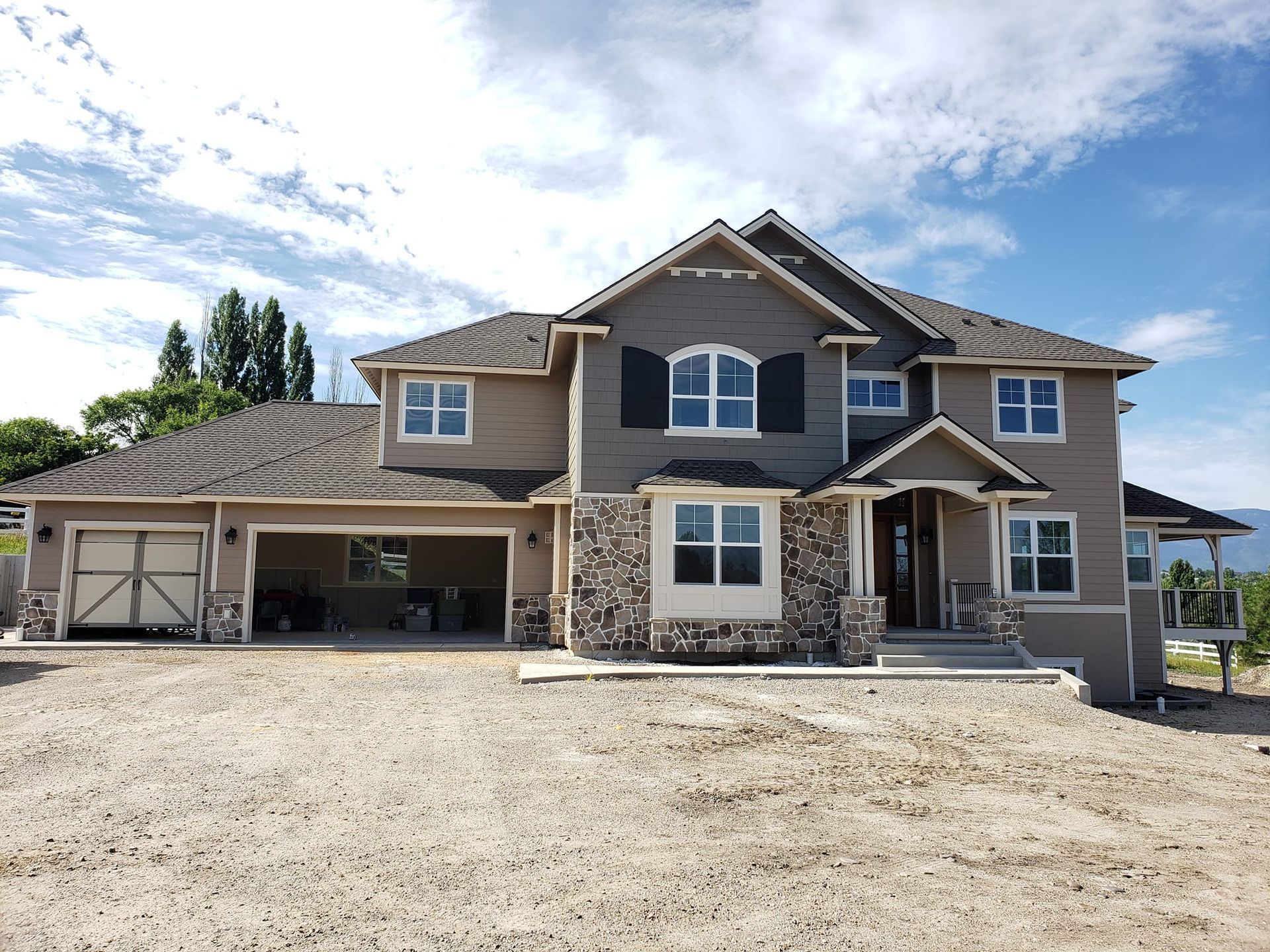 Modern beige barn-style building with dark roof and large garage doors on a gravel lot under a blue sky