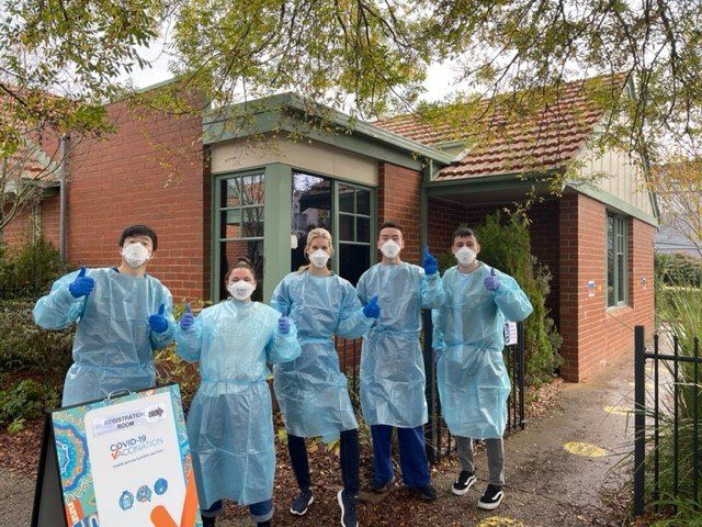 Clinicians in PPE giving a thumbs up and standing in front of the clinic