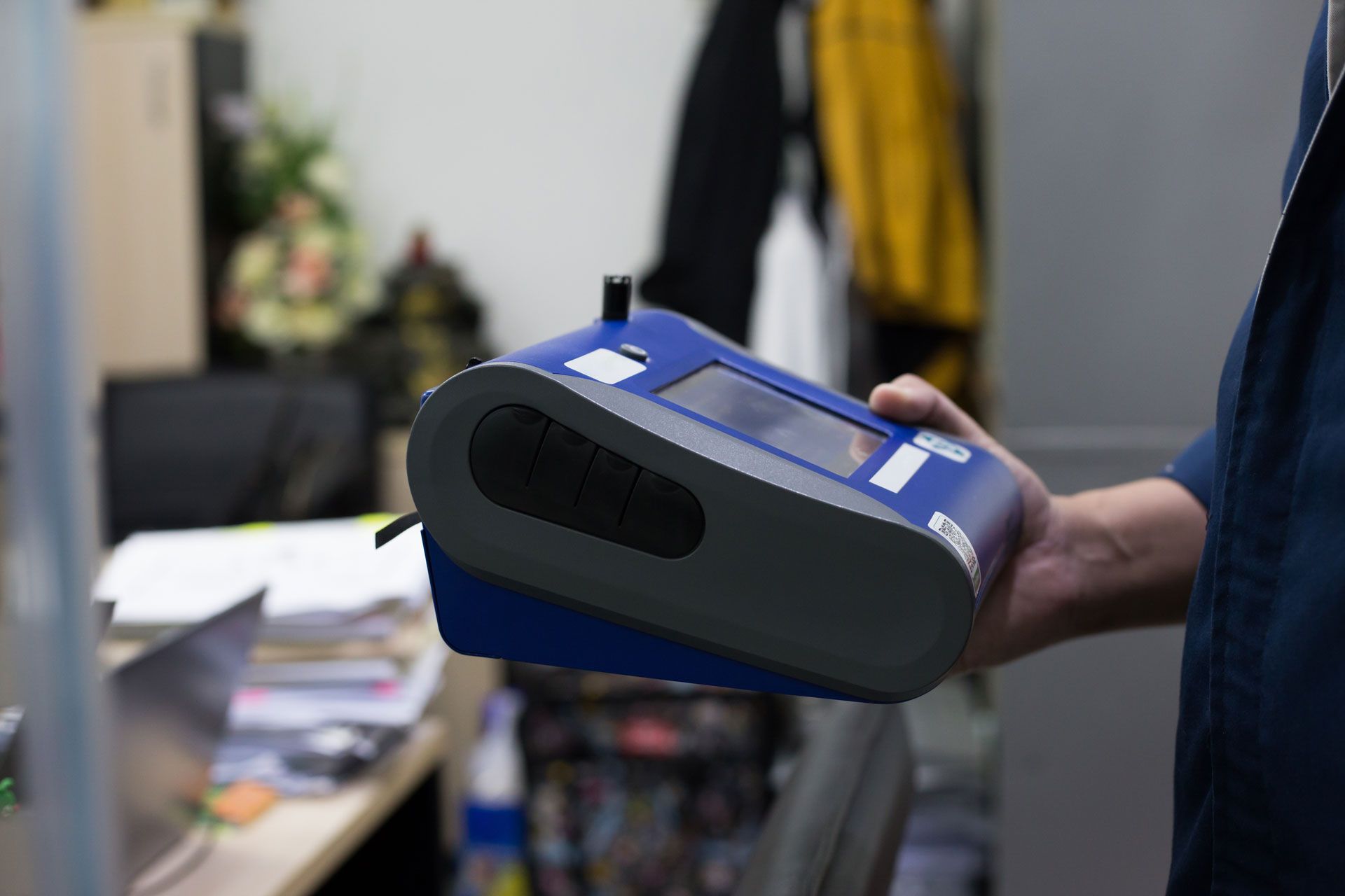 Person holding a blue-and-black handheld device in an office setting.
