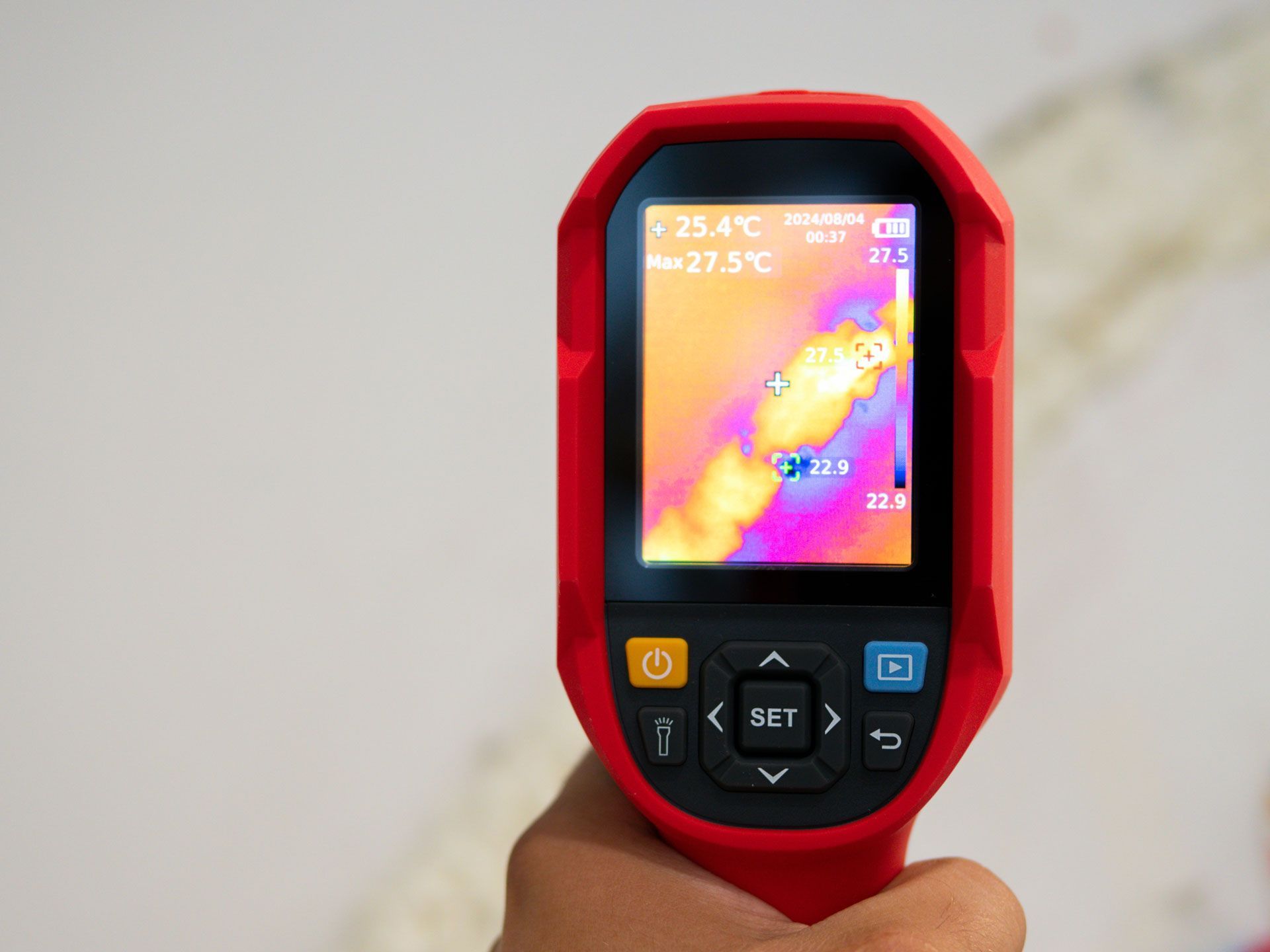 Handheld thermal camera displaying a heat map on its screen, held in a hand
