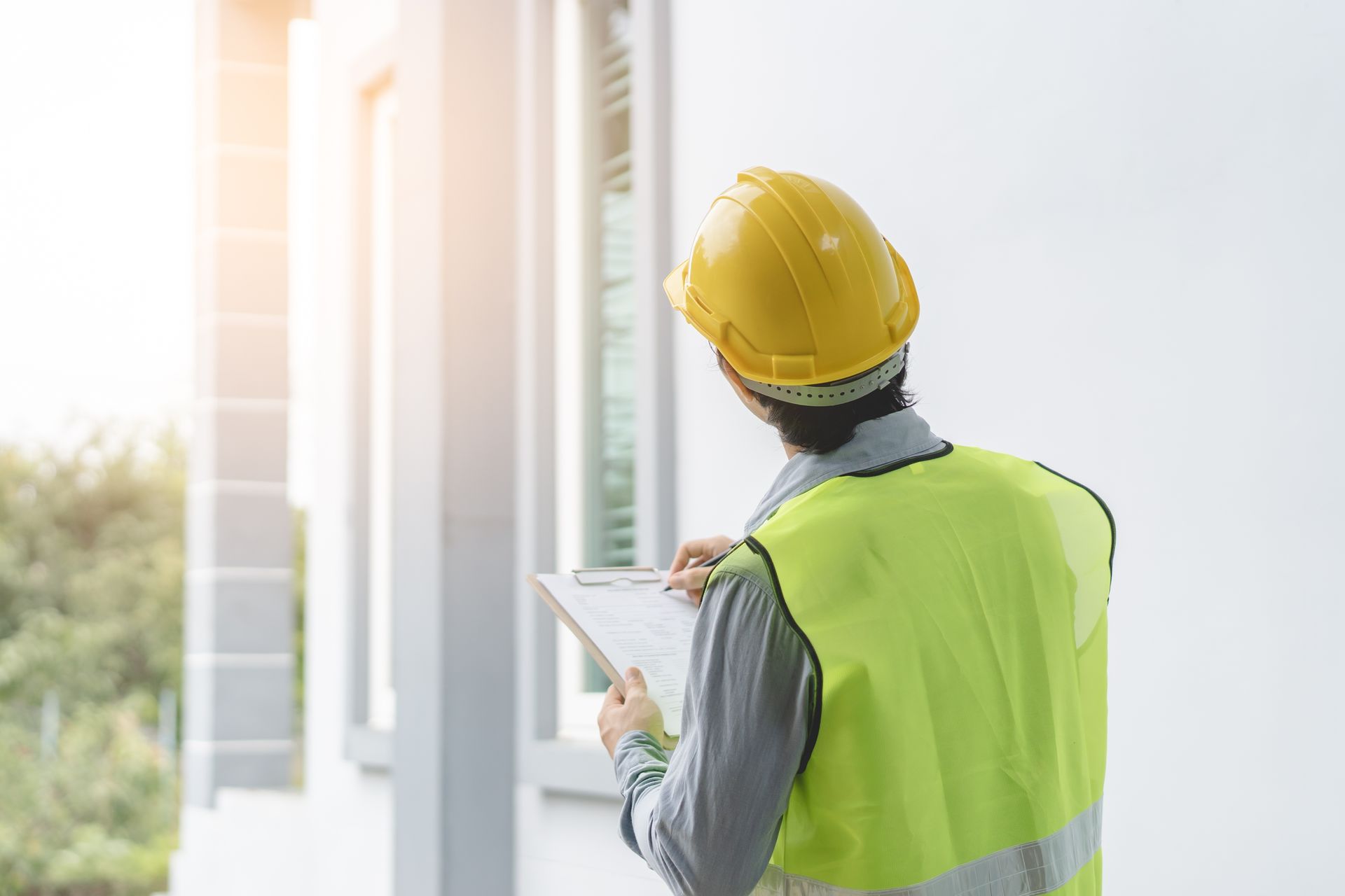 Construction worker in yellow hard hat and safety vest reviewing plans outside a building