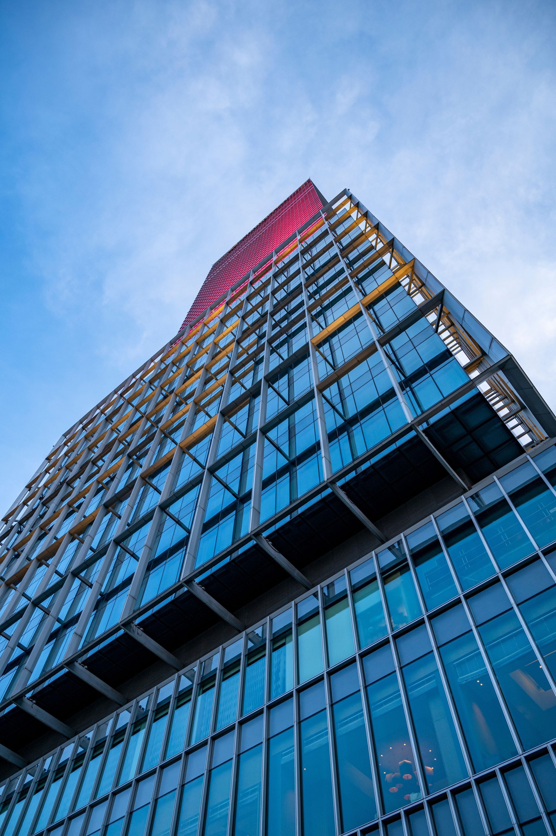 Low-angle view of a modern glass skyscraper with blue sky and red-lit top floors