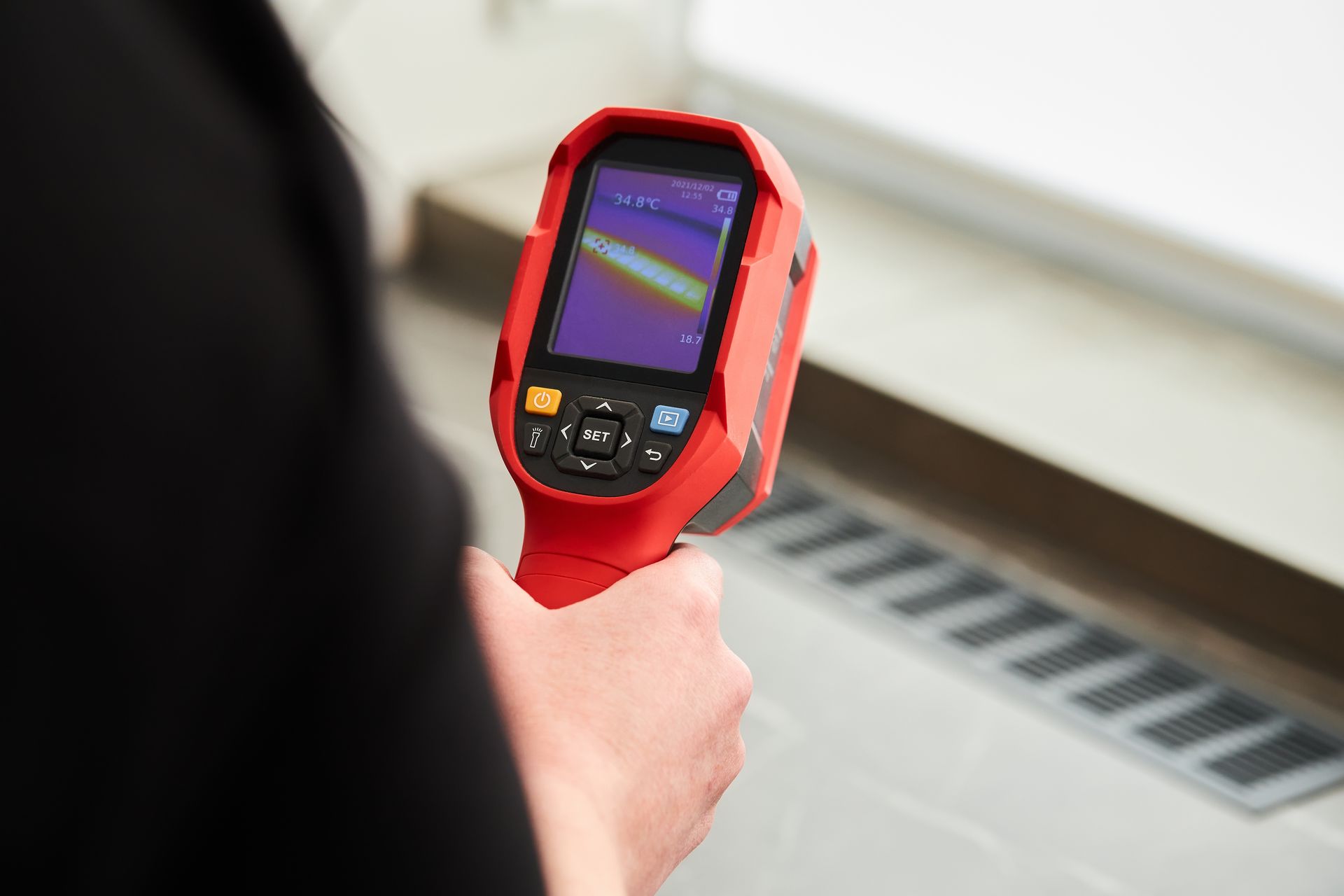 Person holding a red infrared thermometer aimed at a radiator or heating vent.