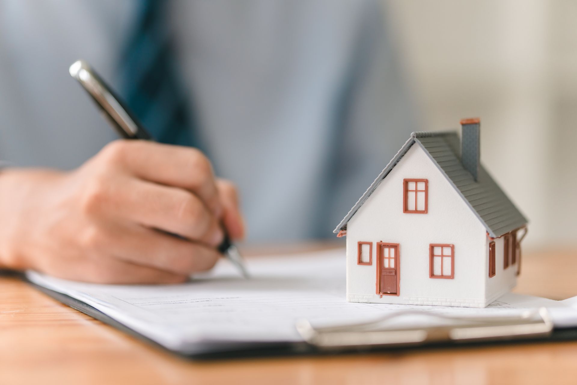 Hand writing on a notebook beside a small house model on a desk