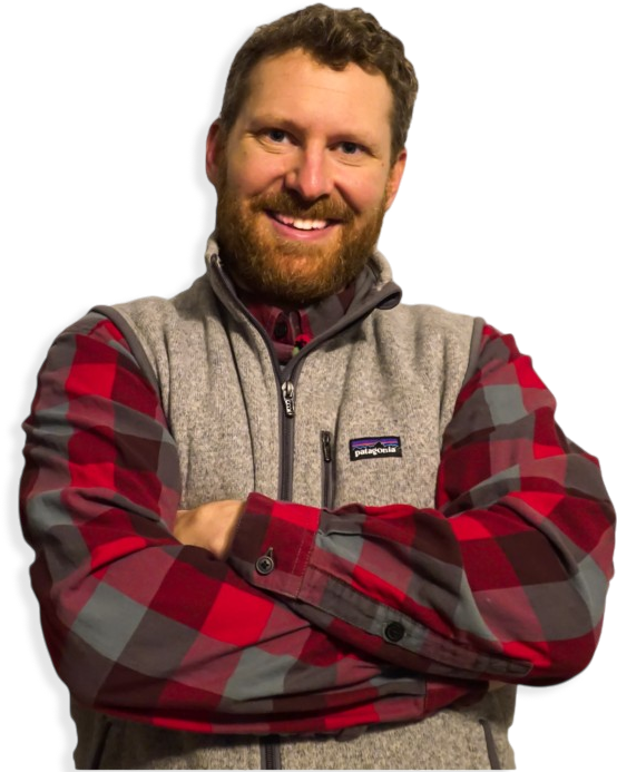 Smiling person with a beard in a red plaid shirt and gray vest, arms crossed, against a white background