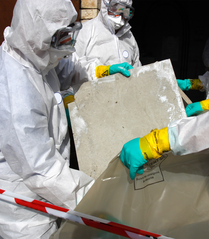 Workers in white protective suits handle large concrete slabs during cleanup or inspection.