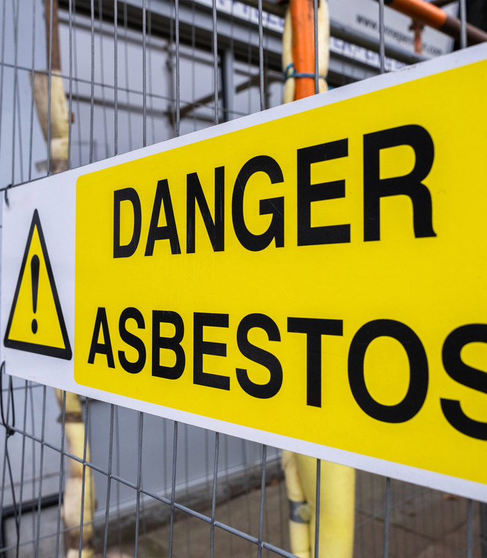 Yellow danger asbestos warning sign on a metal fence at a construction site