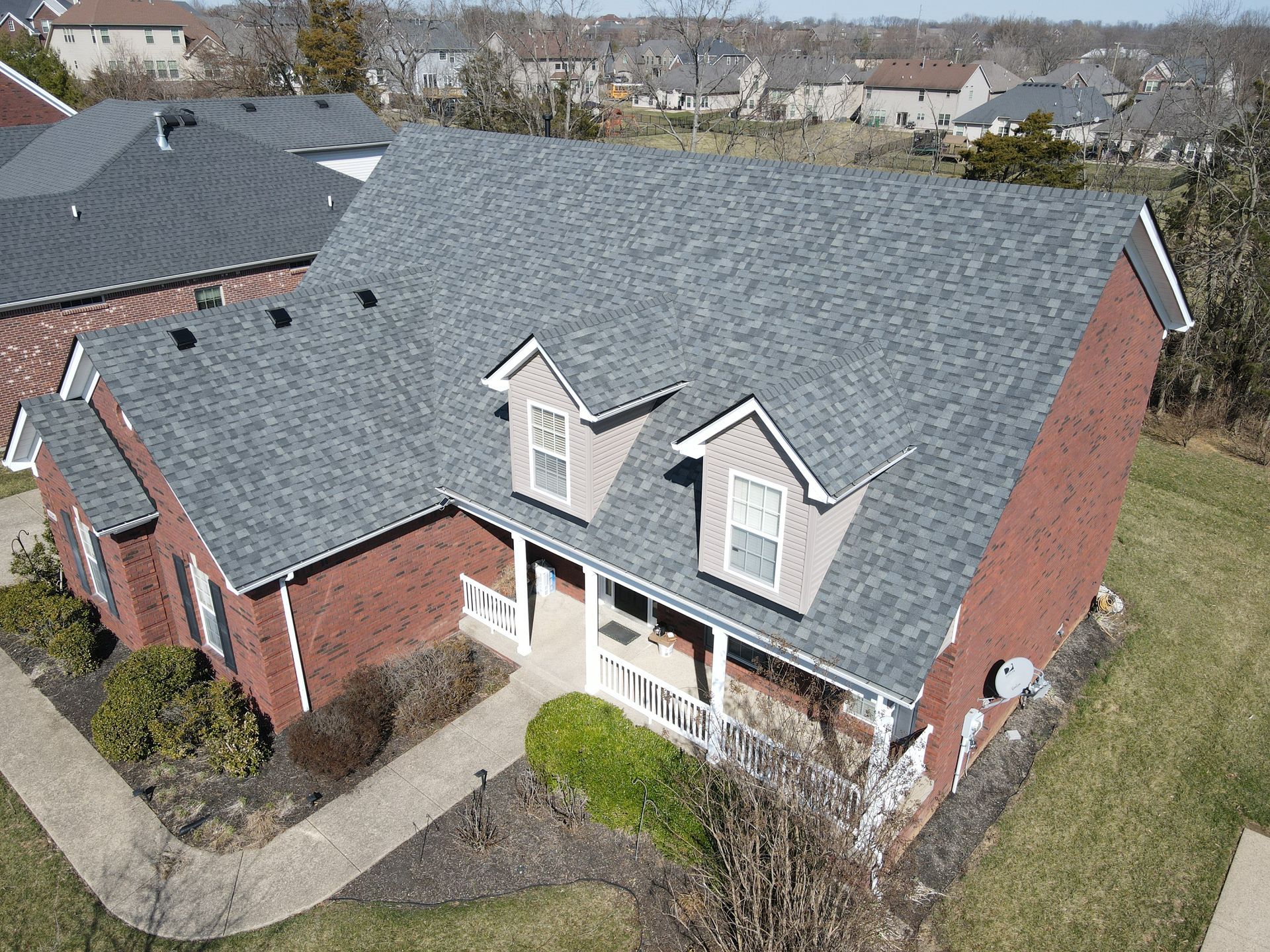 Red brick house with gray roof, two dormers, and a small porch.