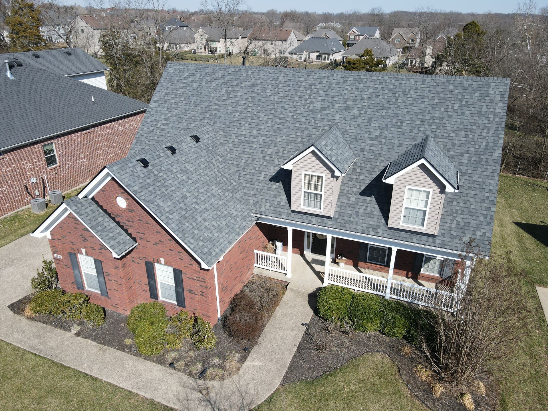 An aerial view of a brick house with a gray roof and a porch.