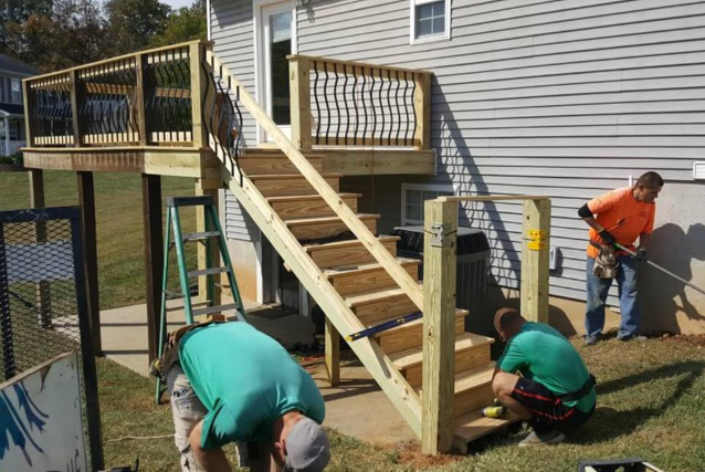 Workers build deck stairs and framing beside house during Deck Building Services in Buckeye, AZ for safe outdoor access.