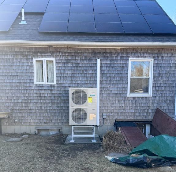 House exterior with rooftop solar panels and a dual outdoor HVAC unit below a window