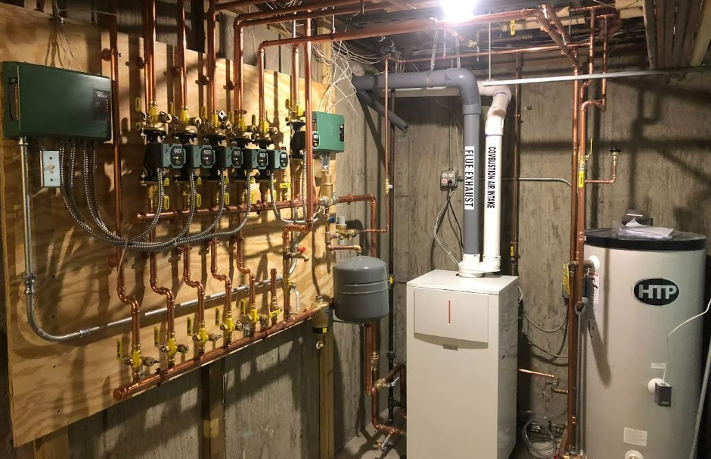 Basement utility room with copper pipes, valves, a white boiler, and a water heater.