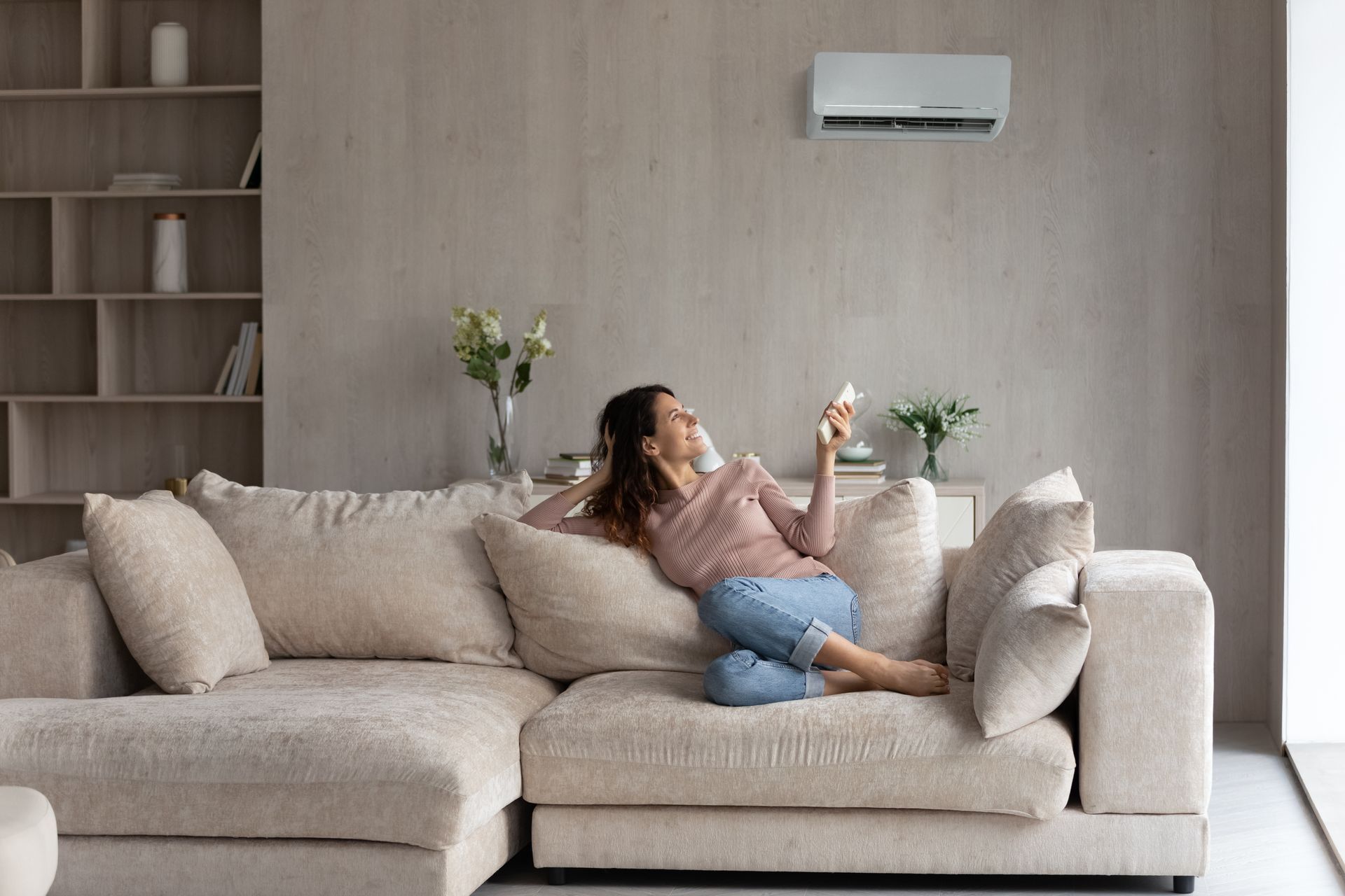 Person lounging on a beige sofa in a minimalist living room with a wall-mounted air conditioner.