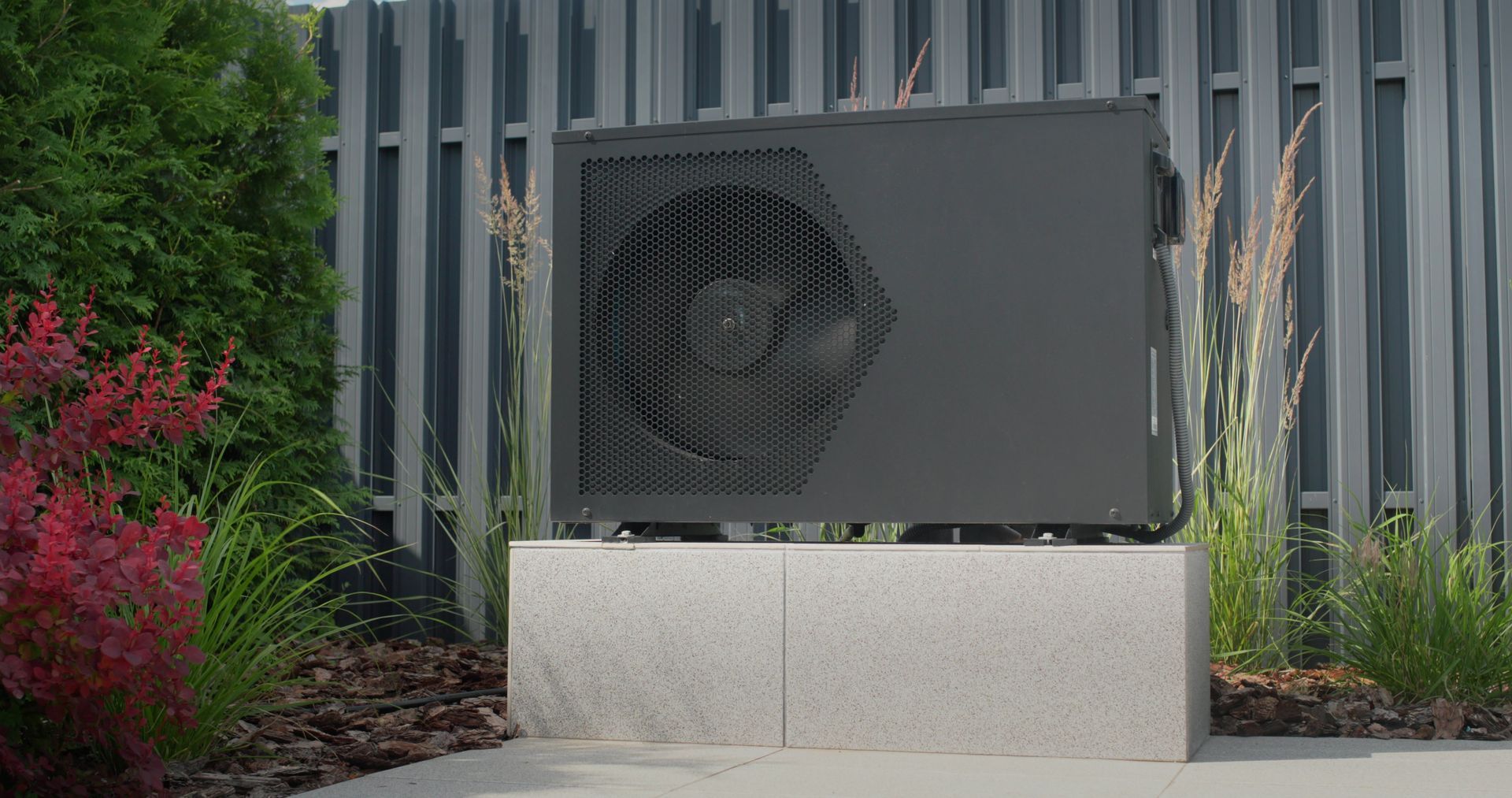 Black wall-mounted vent box on a concrete base in a landscaped outdoor setting