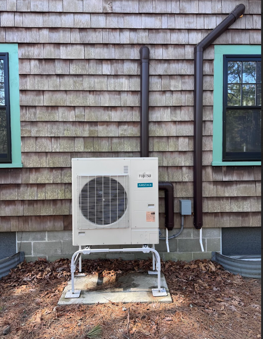 An air conditioner is sitting outside of a house next to a window.