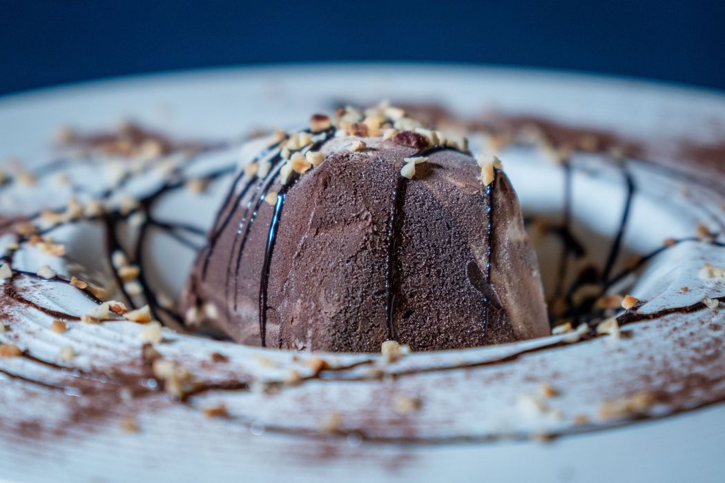 Piatto da dessert con glassa al cioccolato e cacao in polvere accanto a un cremoso cappuccino su un tavolo
