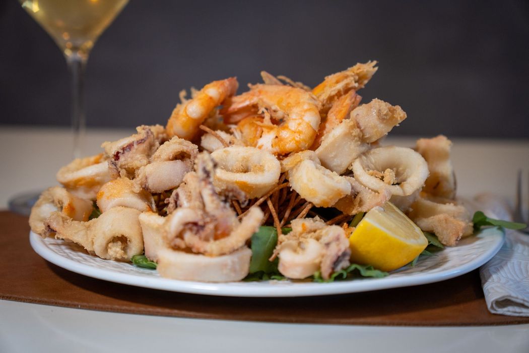 Pesce fritto servito con spicchi di limone ed erbe aromatiche su un piatto bianco.