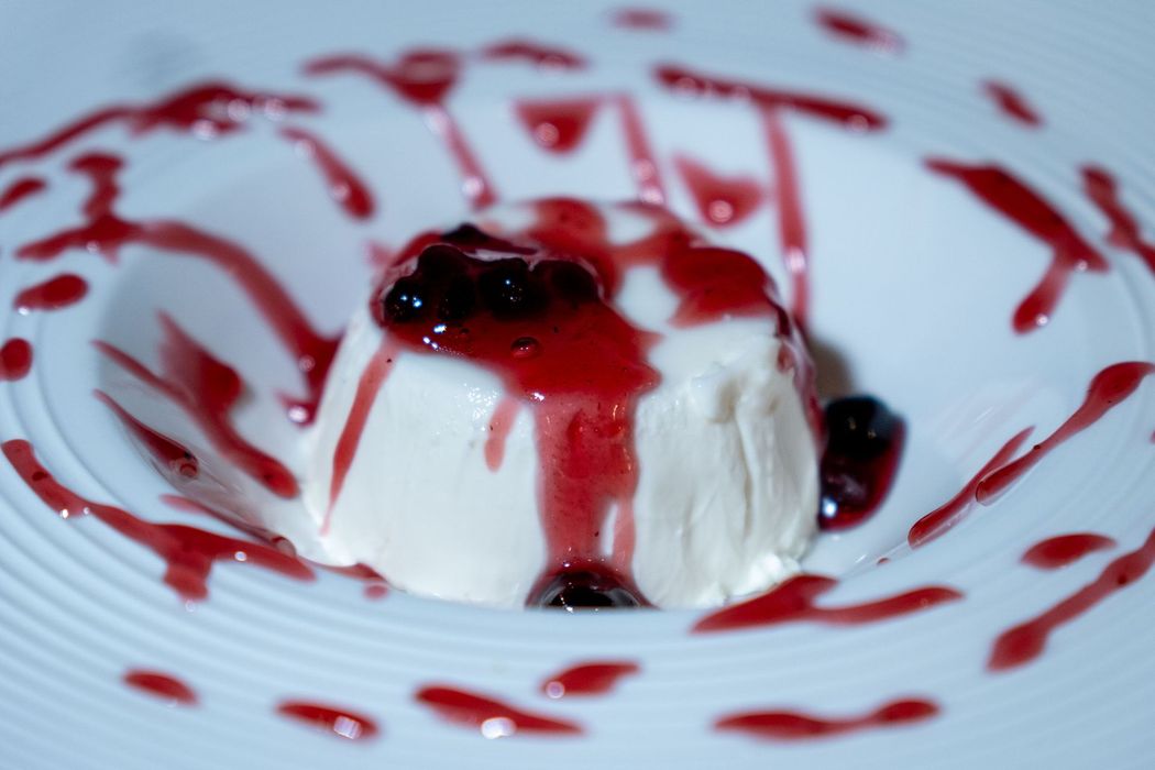 Parfait di dessert guarnito con granola su un piatto bianco, con una spruzzata di cioccolato a lato.