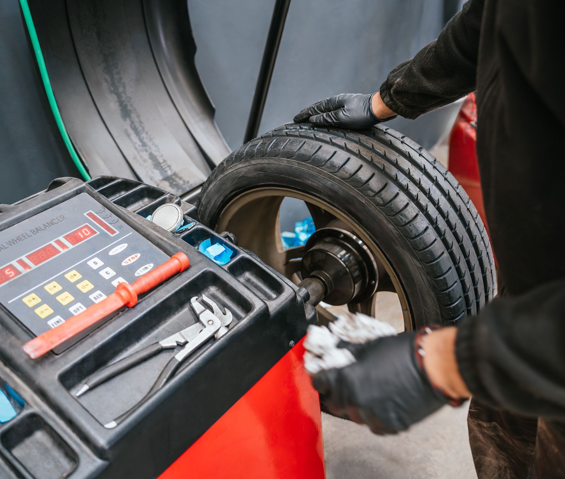 Person balancing a car tire on a machine, wearing gloves in a garage.
