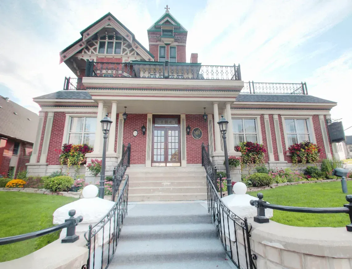Victorian-style brick house with front steps, white columns, and landscaped lawn