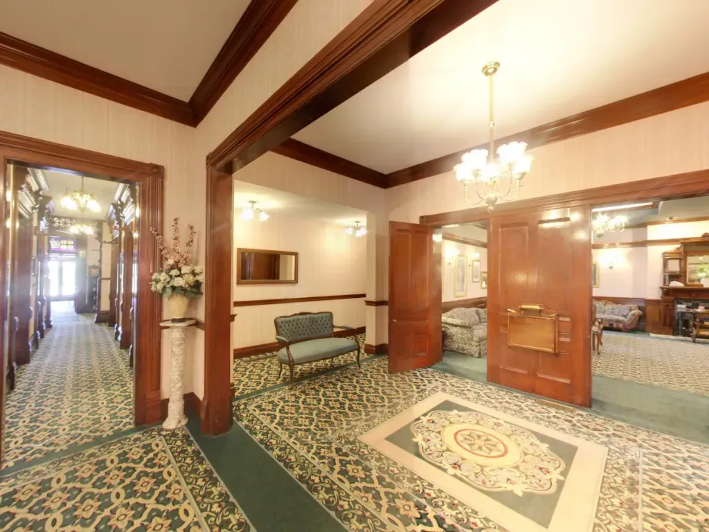 Elegant hotel lobby with patterned carpet, wood beams, chandelier, and open glass doors