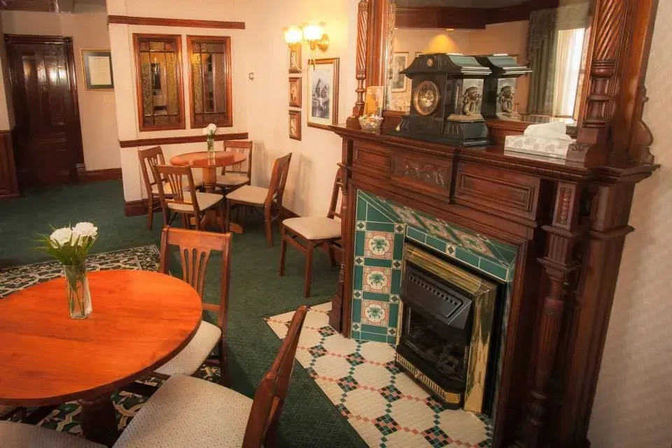Cozy sitting room with ornate fireplace, round wooden table, and green upholstered chairs