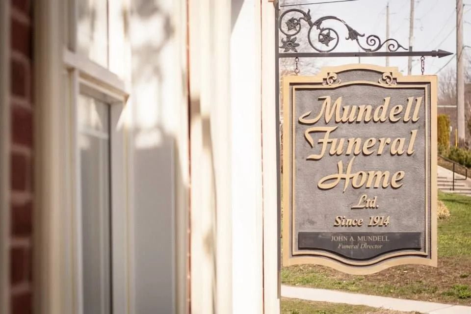 Mundell Funeral Home sign beside a sunlit building entrance