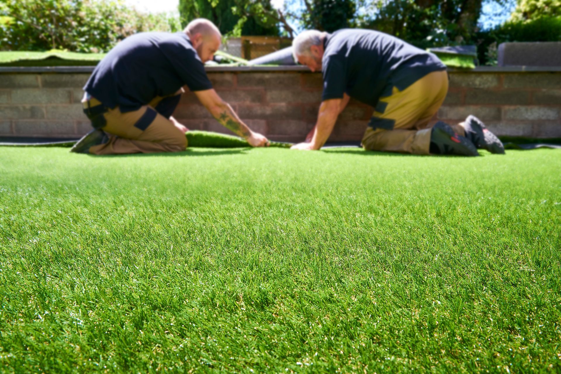 Two men are kneeling on top of a lush green lawn.