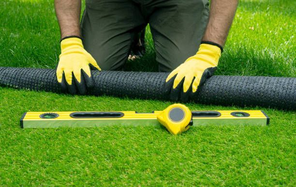 A man is kneeling on the grass with a tape measure and a level.