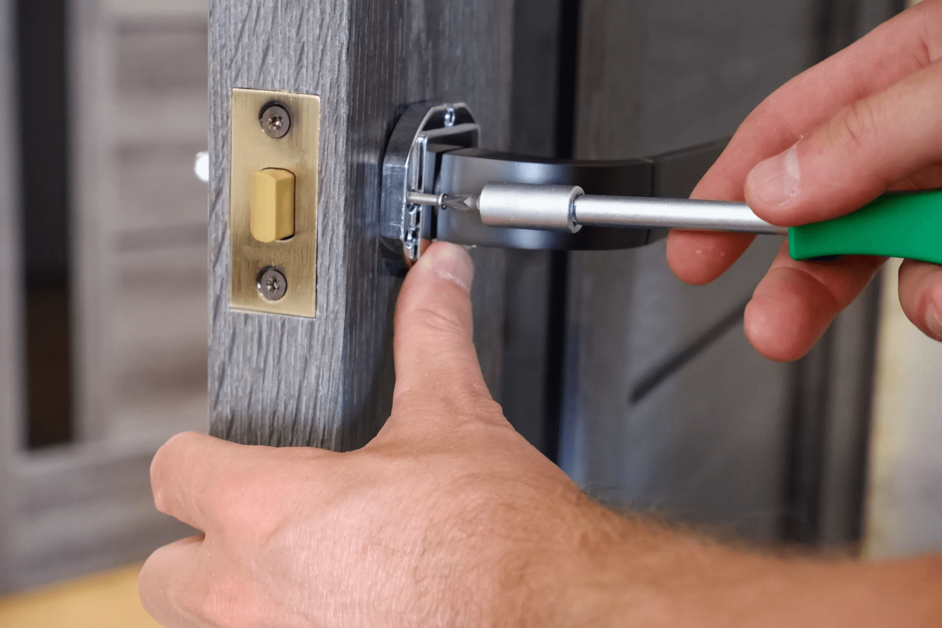 Hands using a screwdriver to adjust a door strike plate on a wooden door