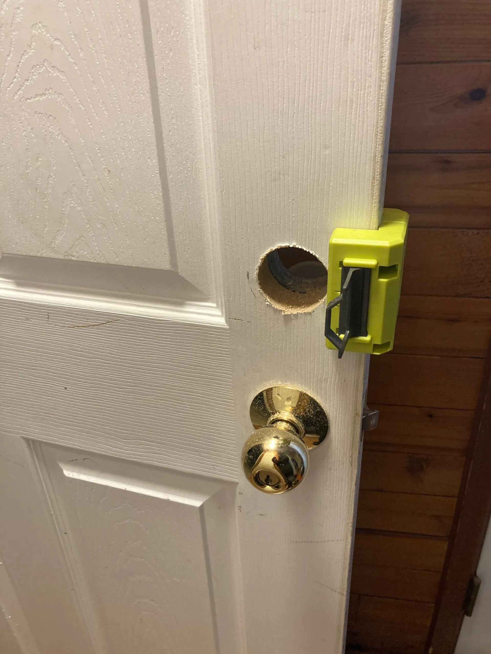 White door with brass knob and an open lock hole, secured by a yellow latch on the side.