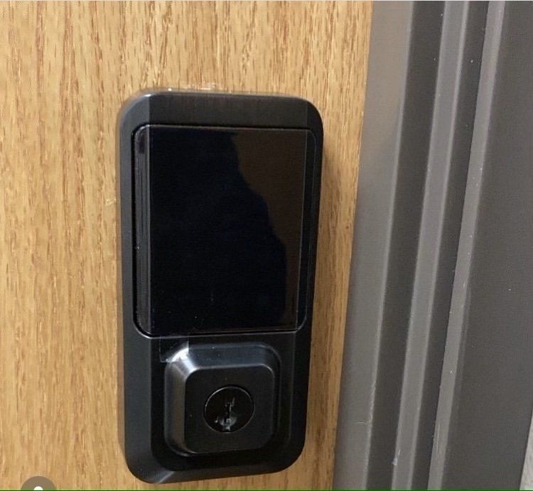 Black smart door lock on a wooden door next to a gray door frame